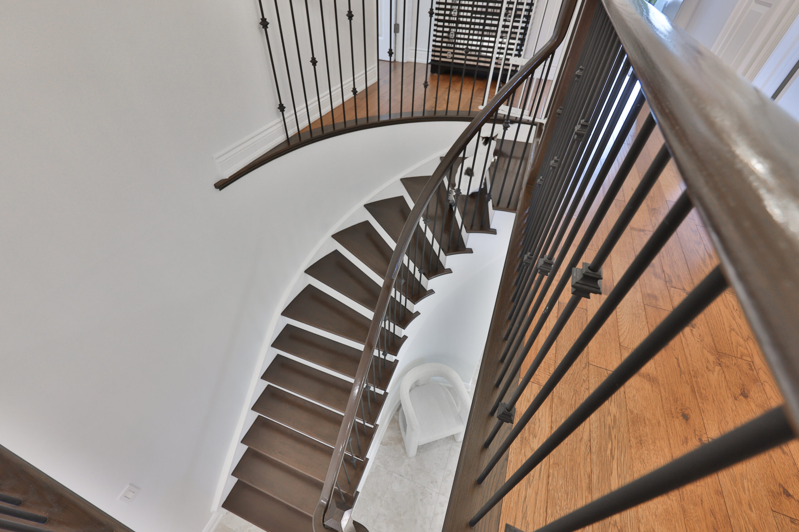 Curved wooden staircase with black railings and white walls