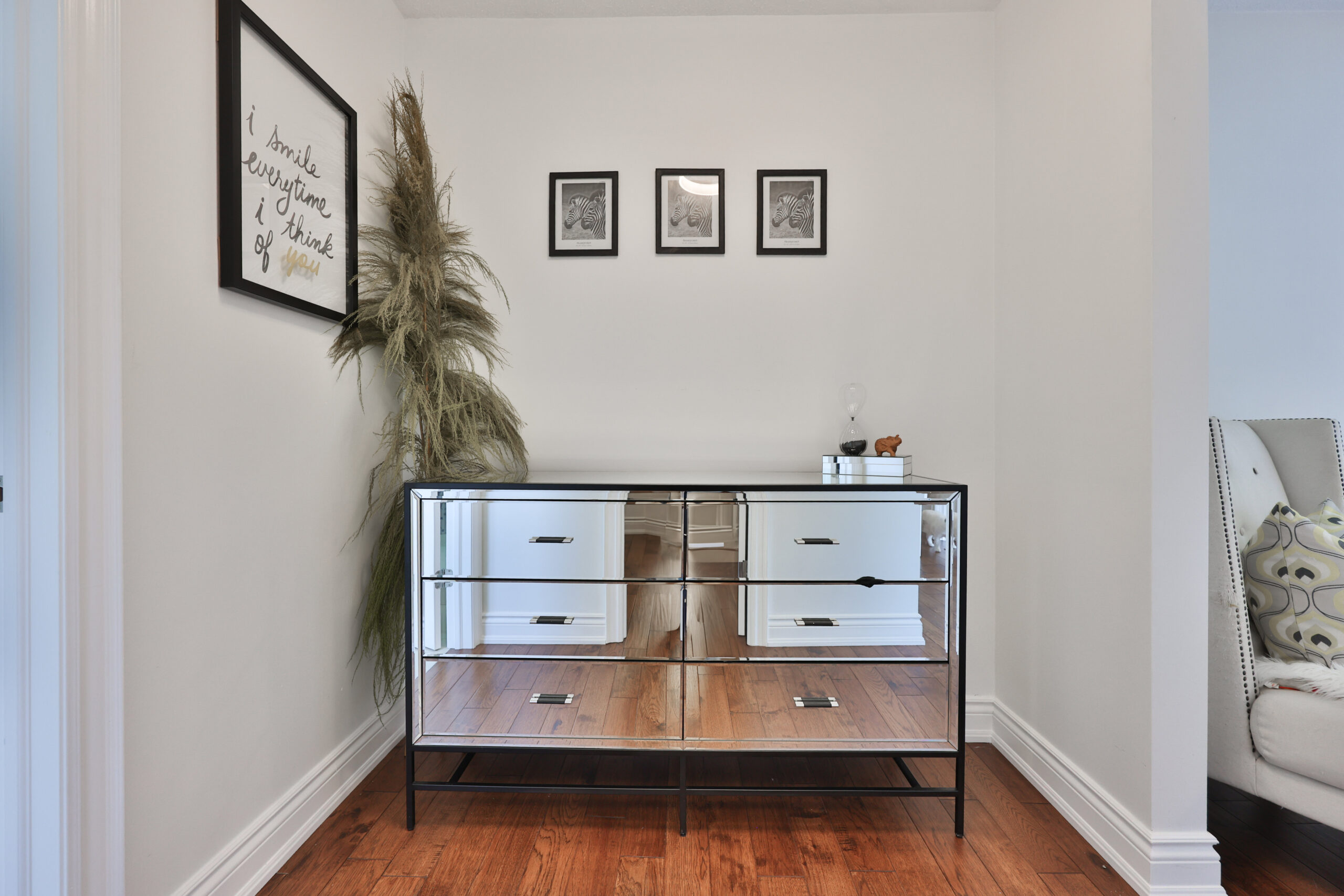 Mirrored dresser against a white wall with framed artwork and a plant
