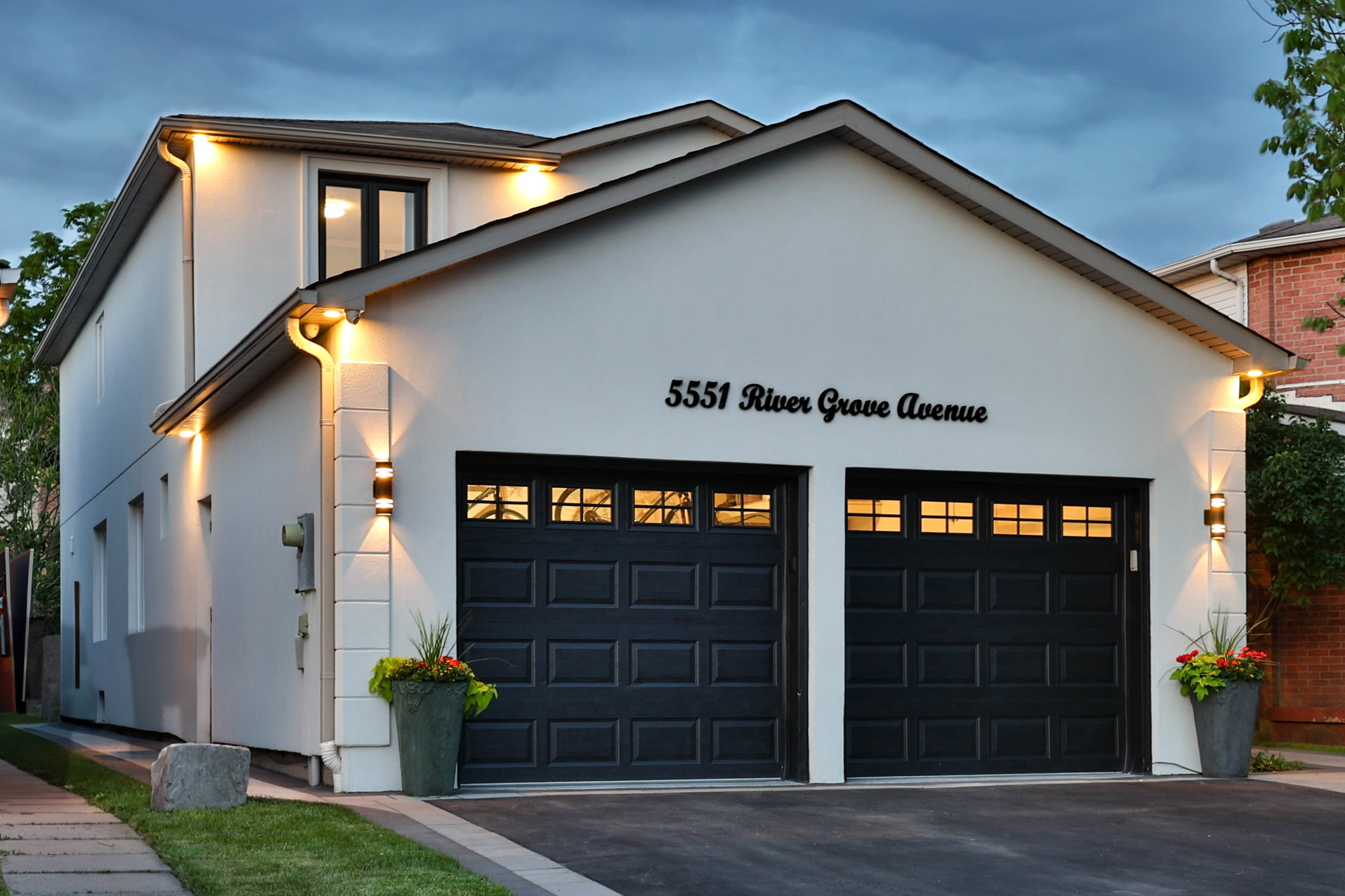 Modern two-story house with black garage doors and illuminated exterior.