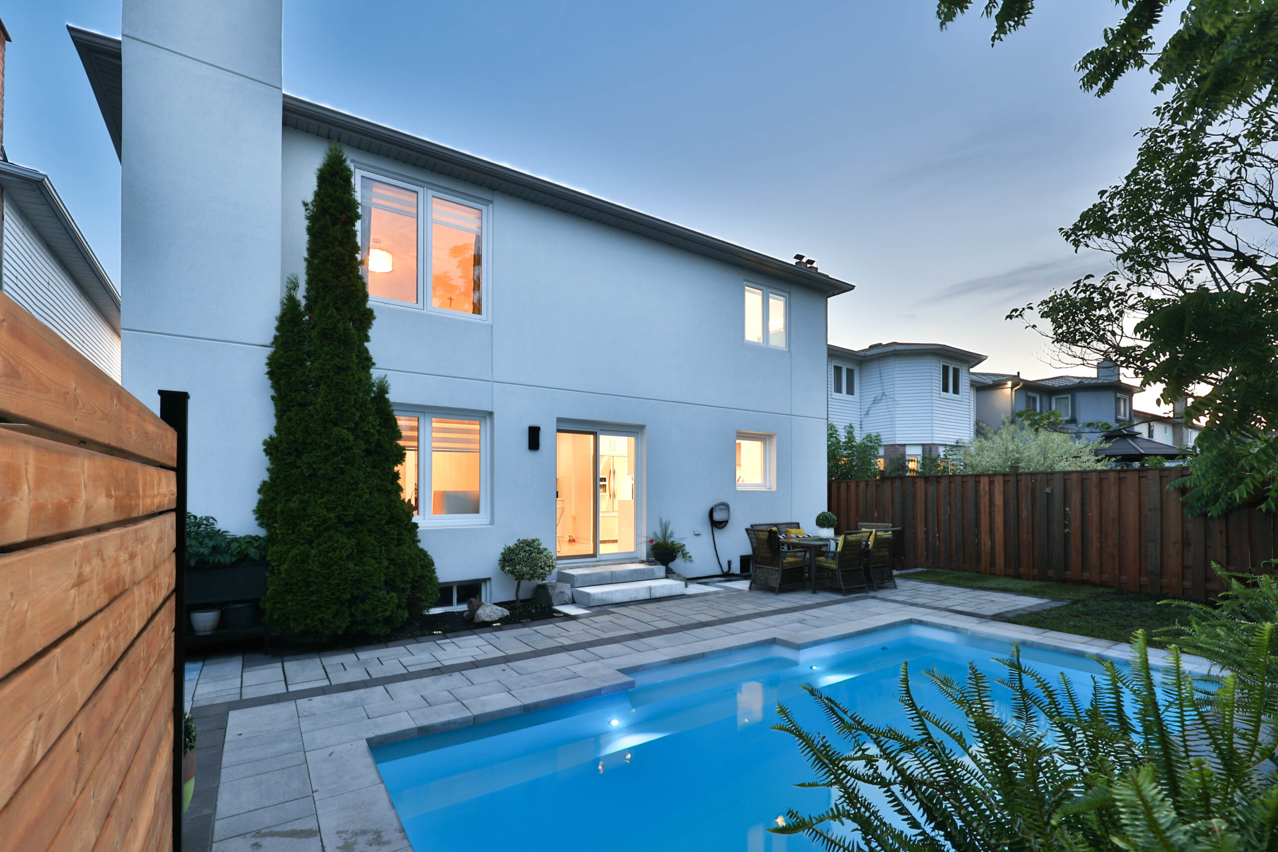 Modern white house with a pool and landscaped yard at dusk