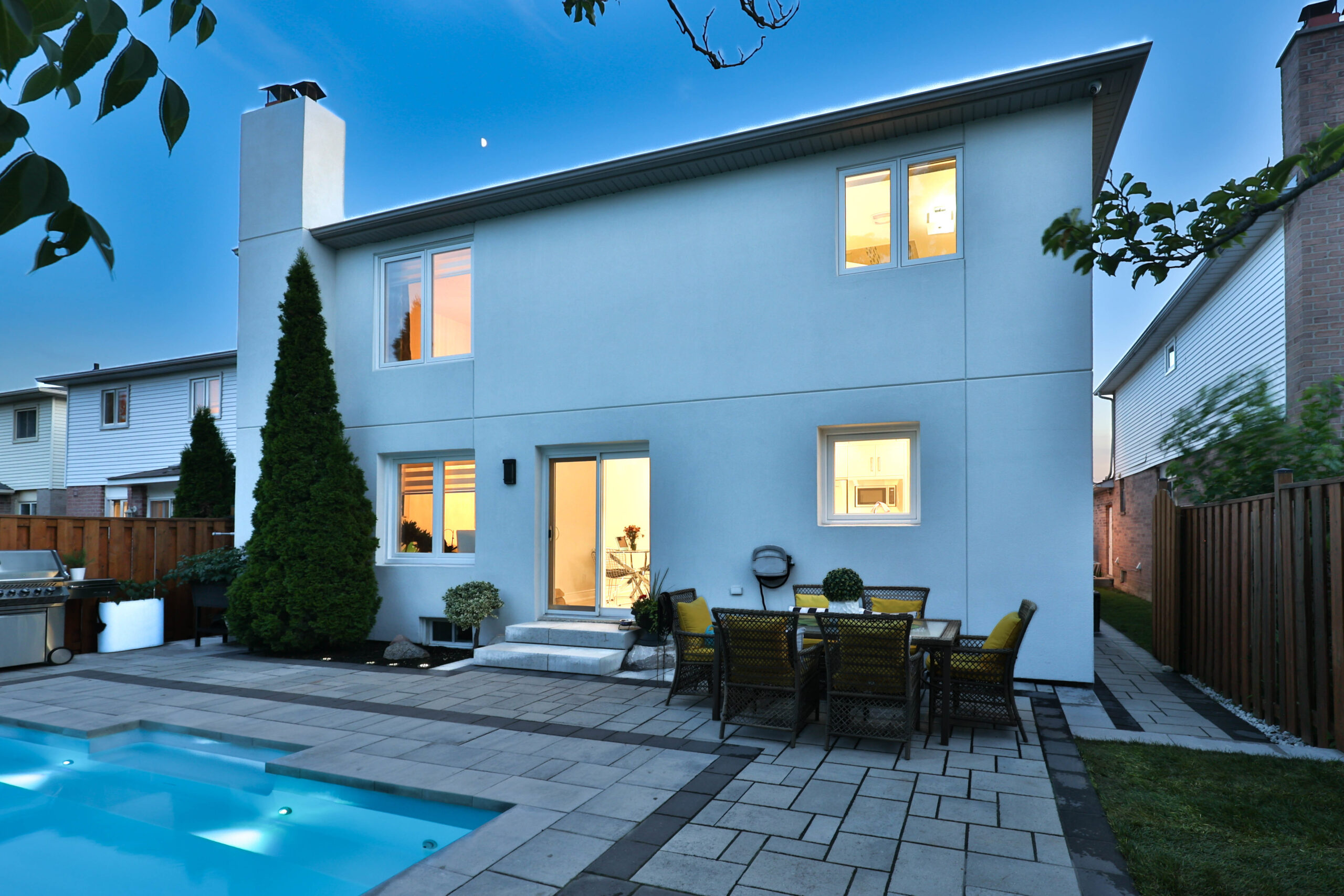 Modern two-story house with a pool and outdoor dining area at dusk