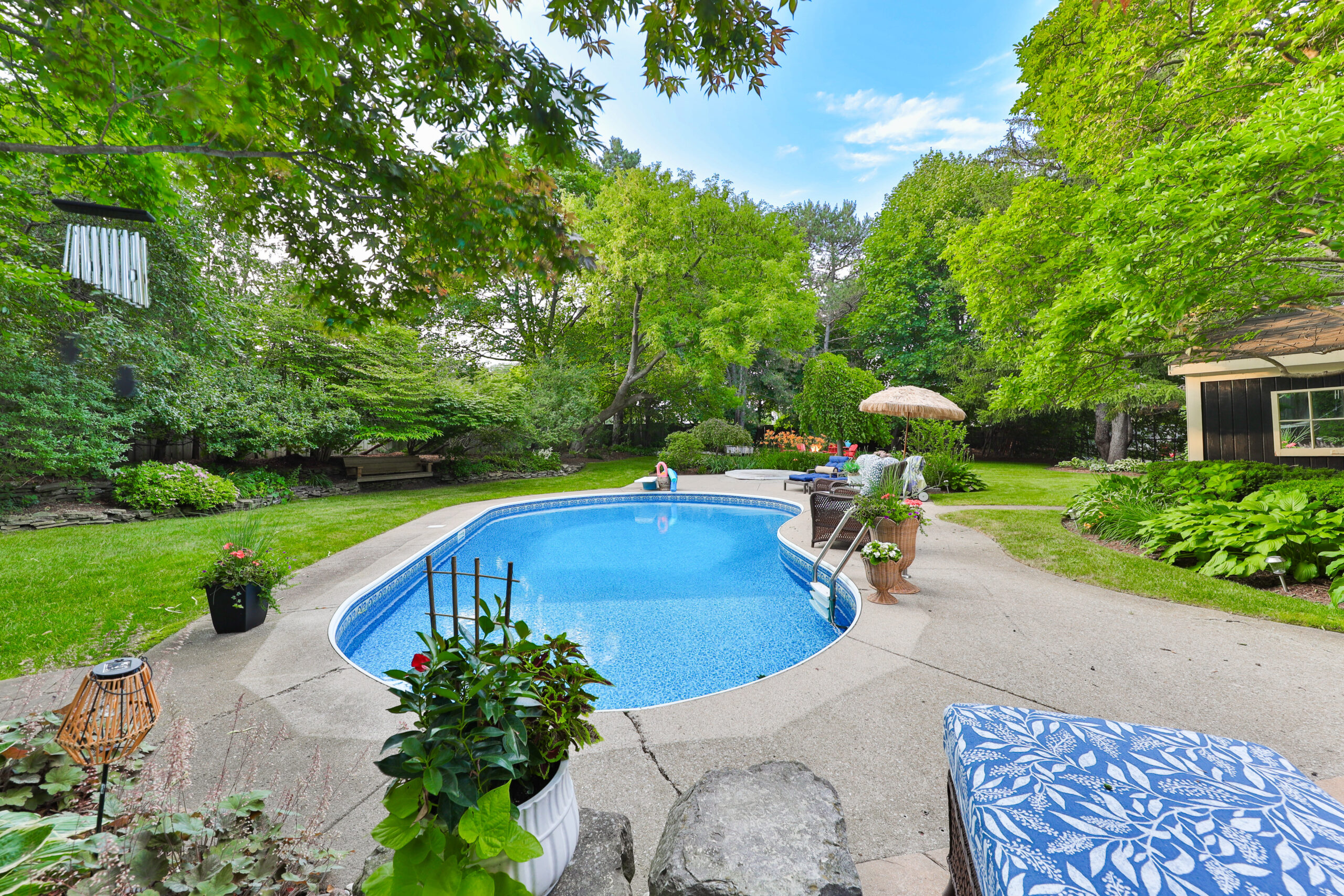 Backyard pool area surrounded by lush greenery and patio furniture