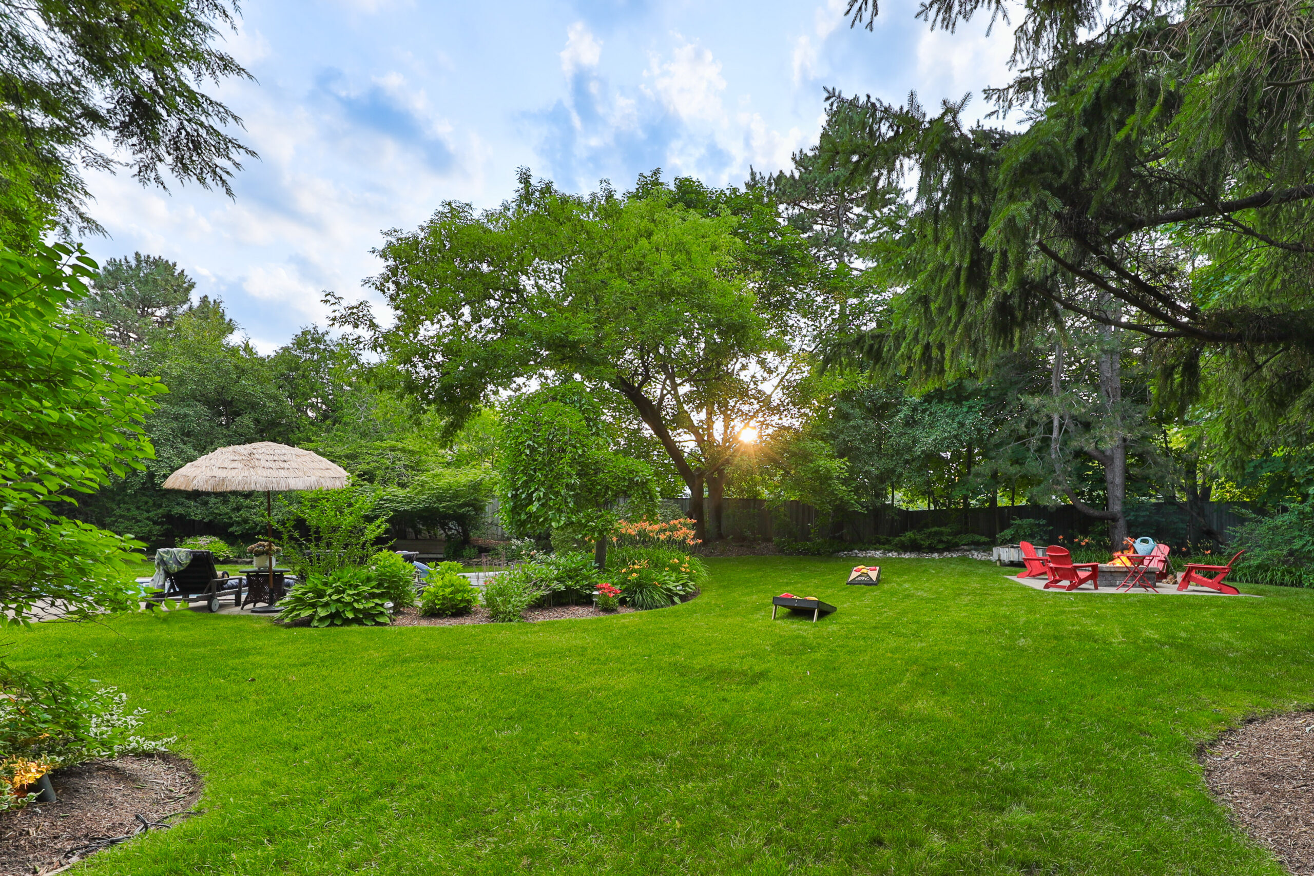 Lush backyard with green lawn, patio furniture, and trees at sunset