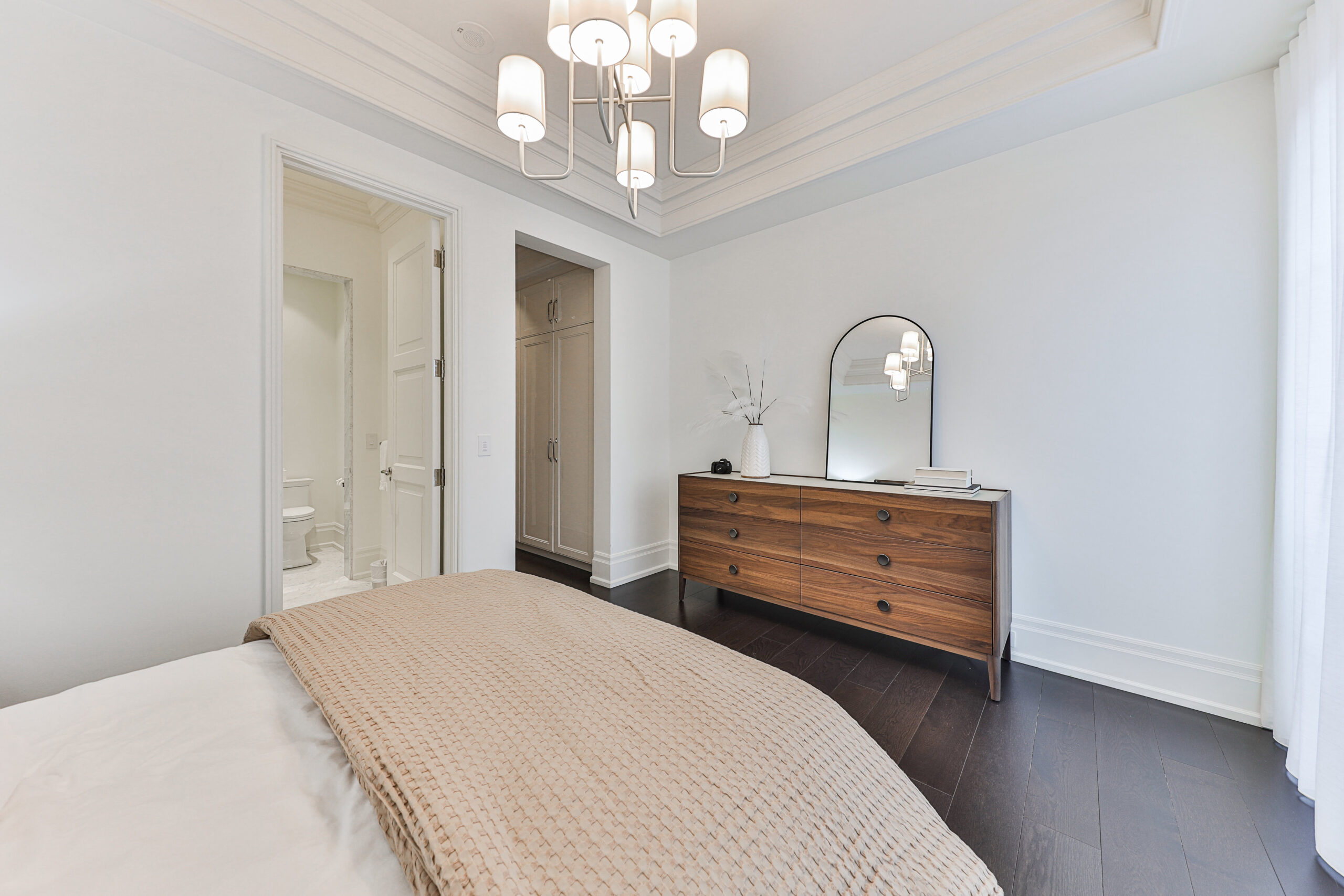 Modern bedroom with a chandelier, wooden dresser, and neutral decor