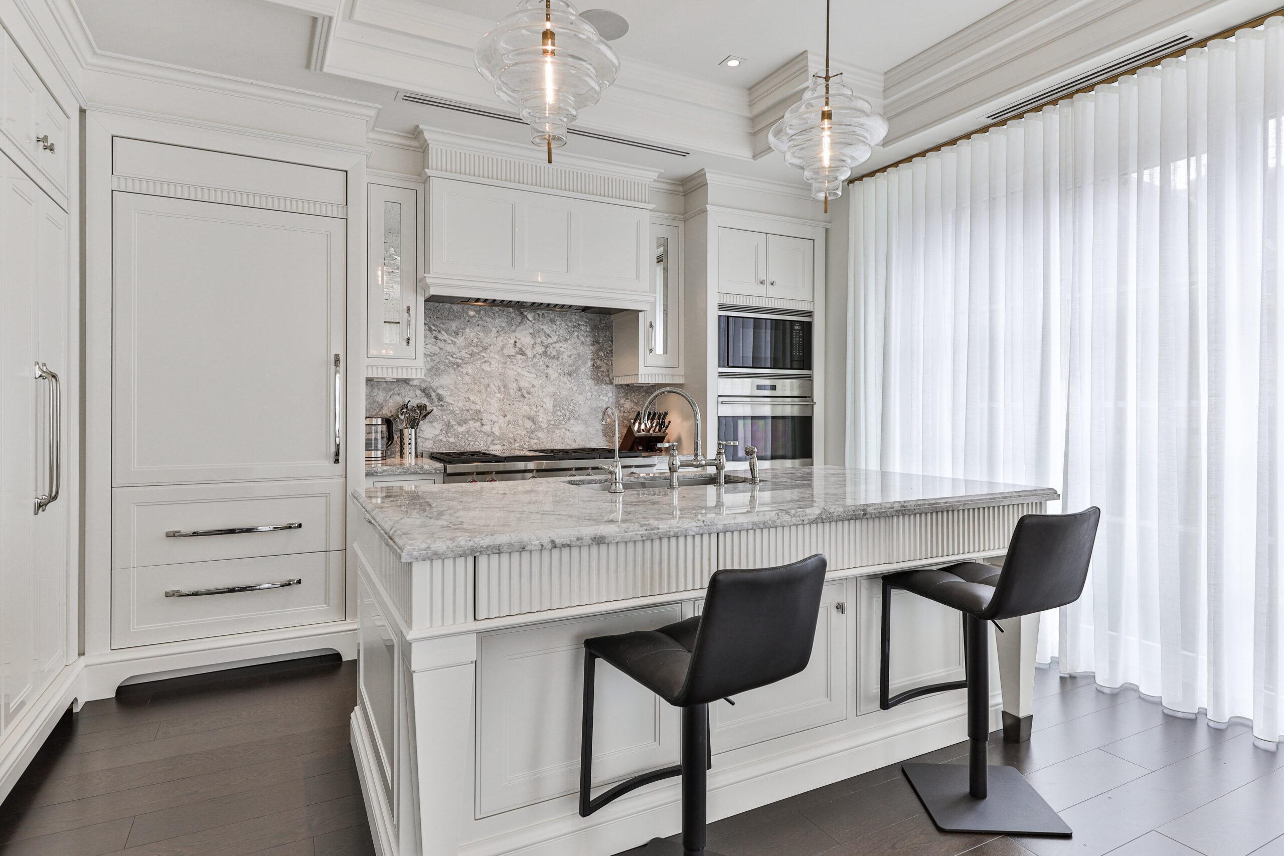 Modern kitchen with white cabinetry, marble countertops, and bar stools