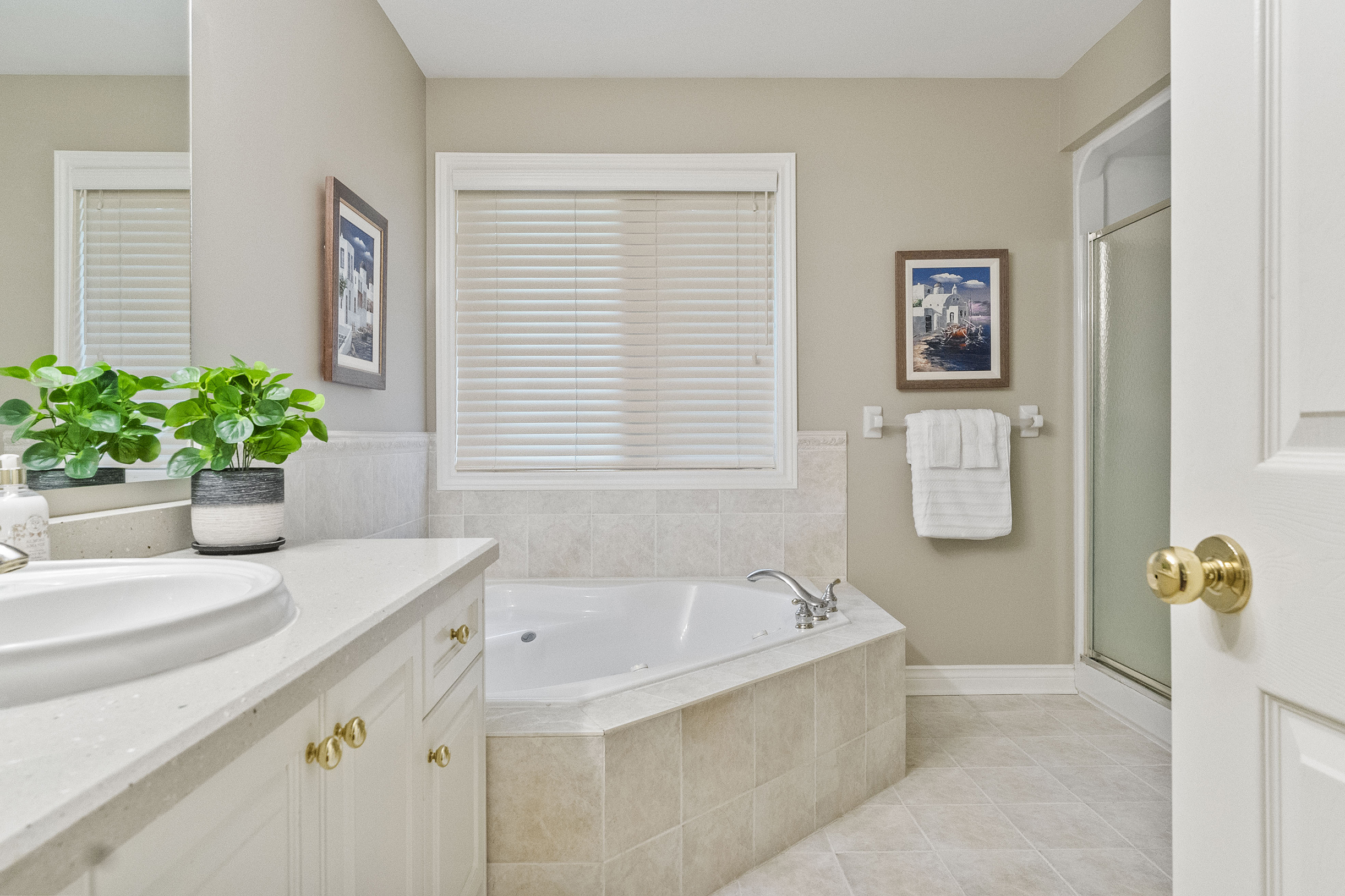 Spacious bathroom featuring a corner bathtub, light-colored walls, and decorative plants