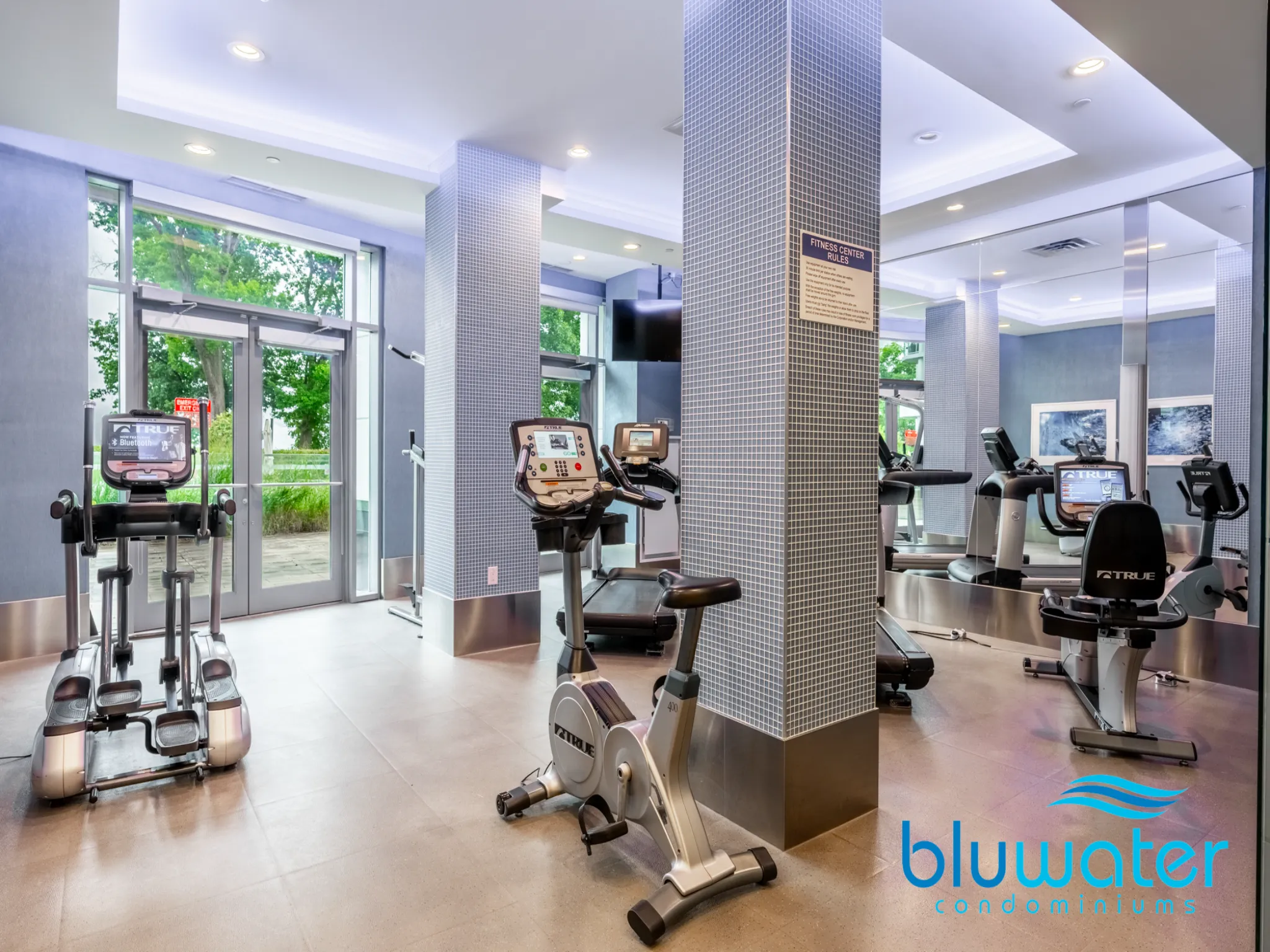 an exercise room with lots of equipment, well lit with grey walls and recessed lighting