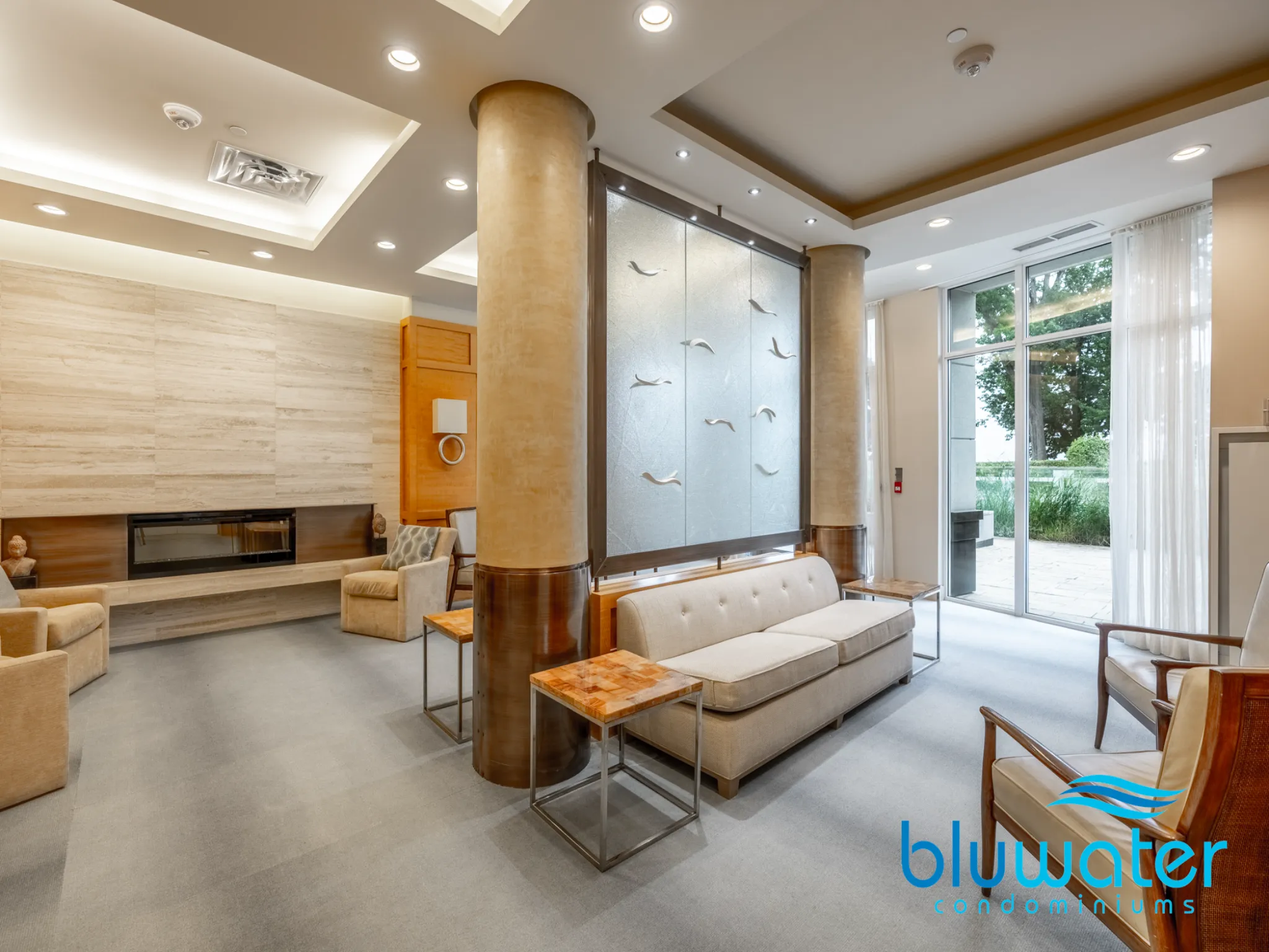 a light room with grey floors and recessed lighting with white couch and leather chairs