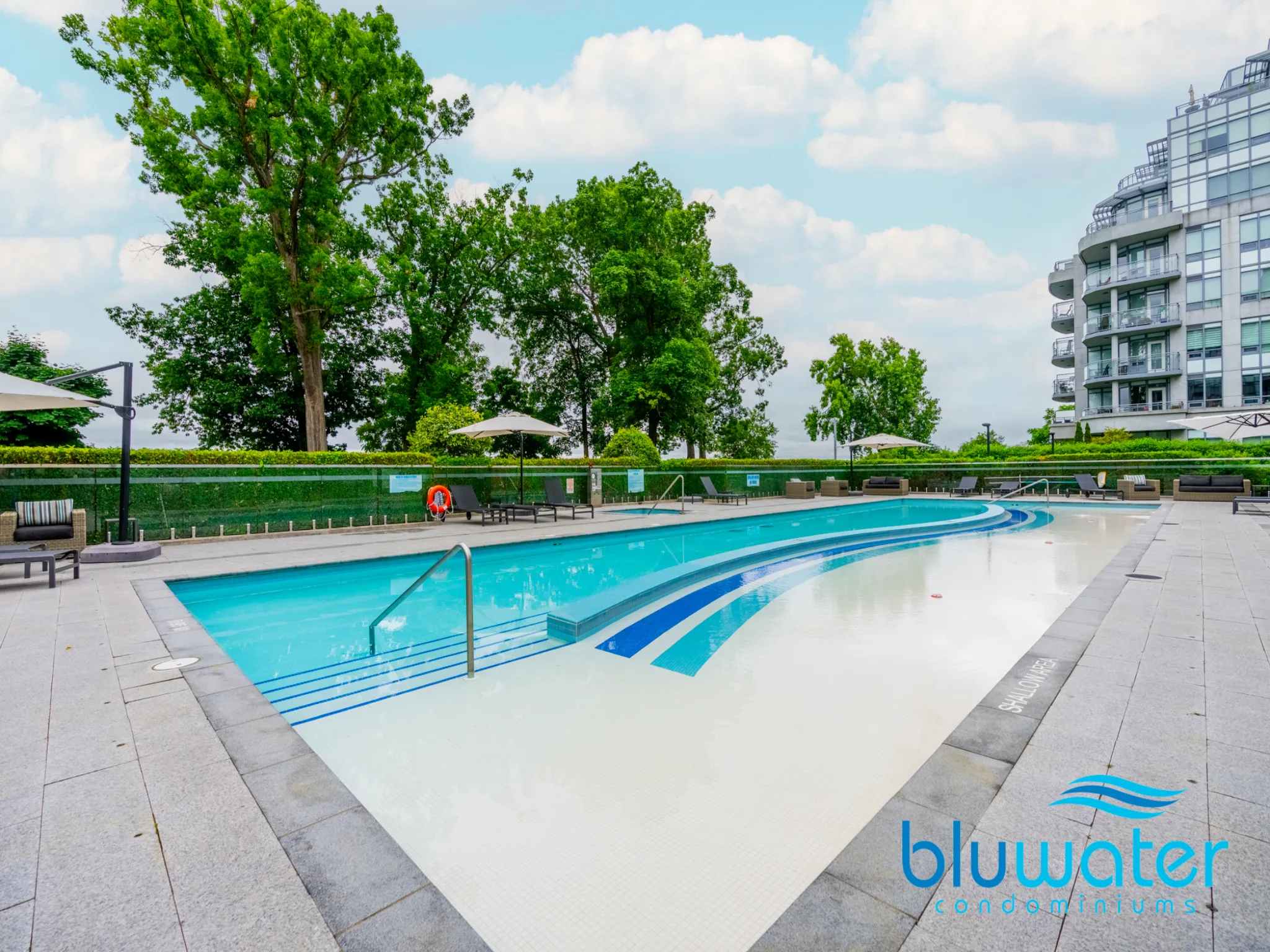 close up view of the pool and pool deck, large trees and building in the background
