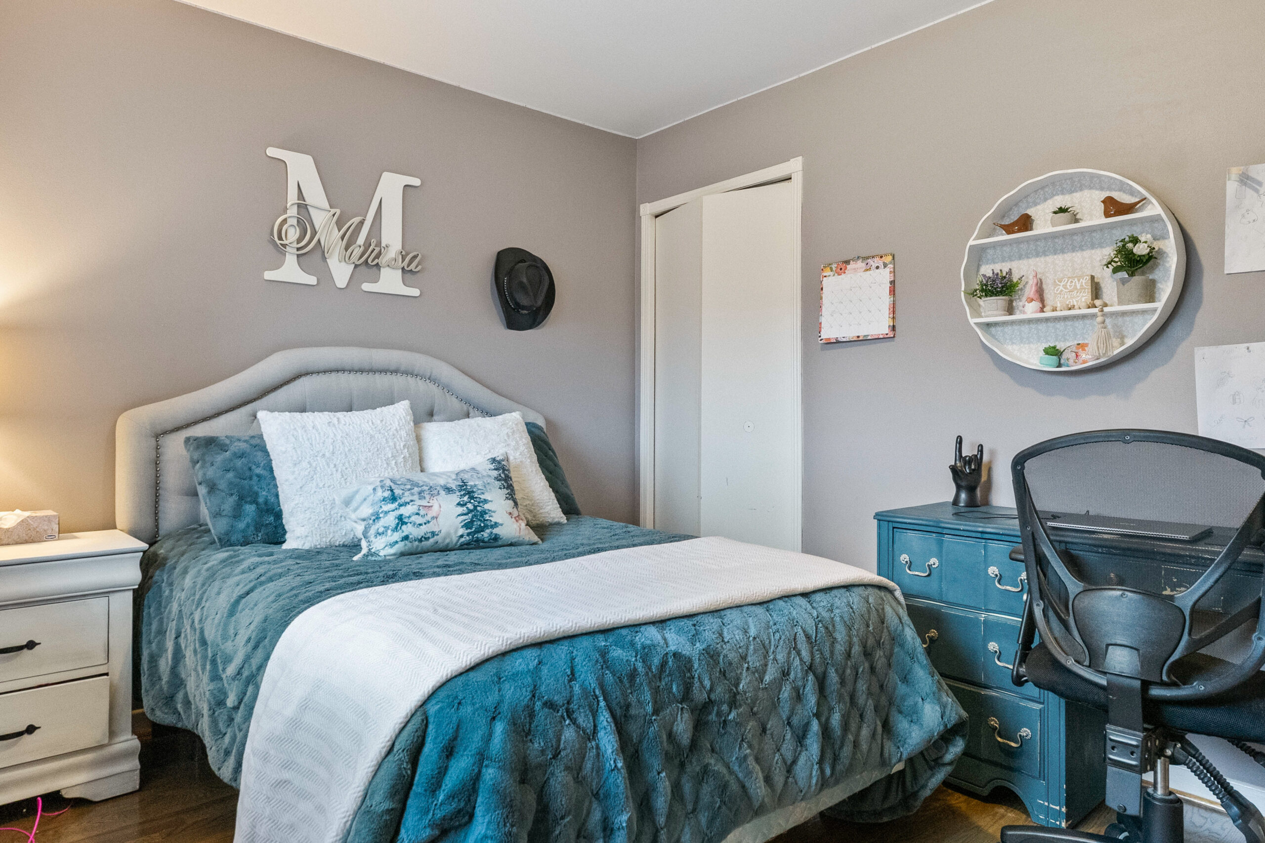 Cozy bedroom with teal bedding, desk, and decorative wall shelves