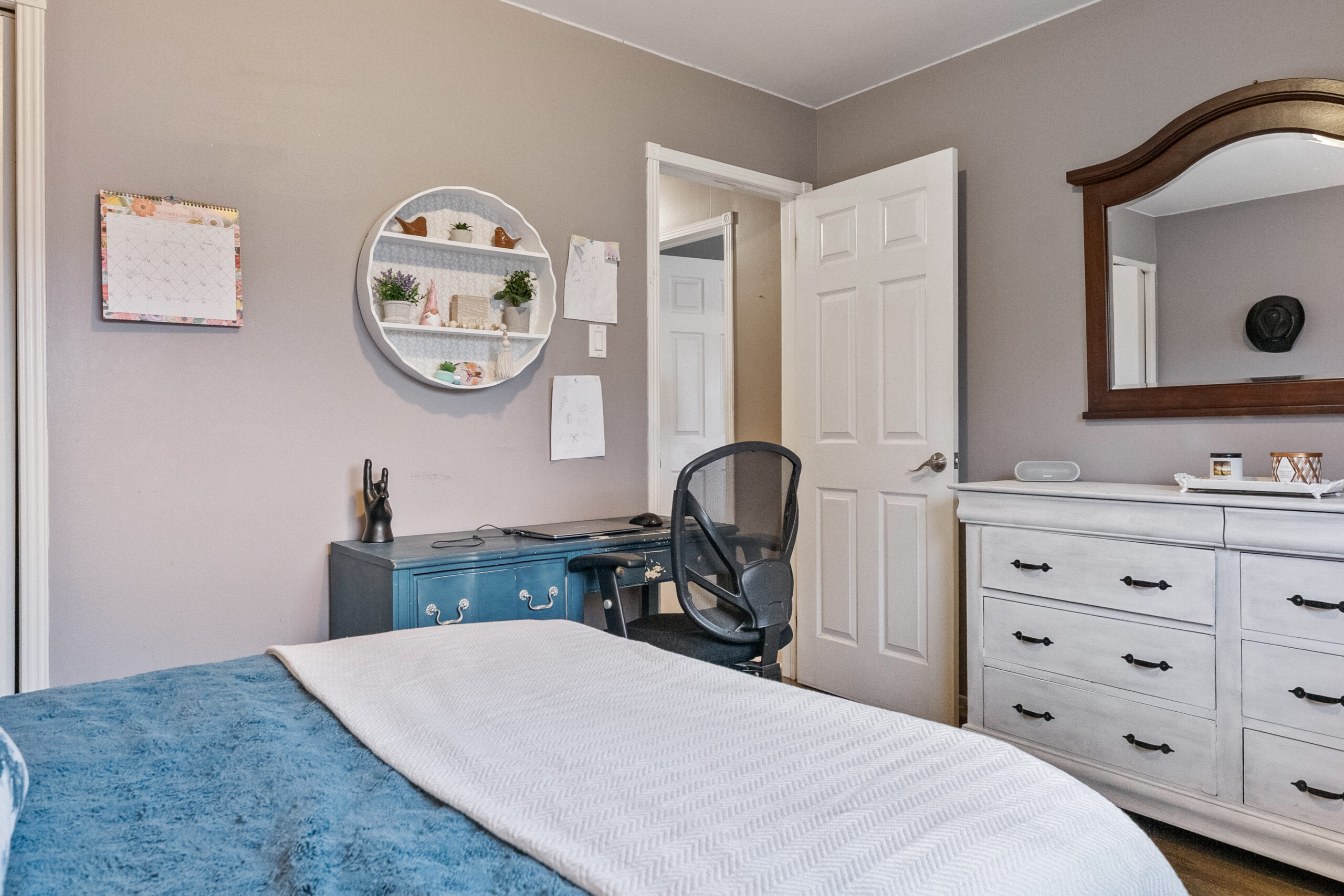 Cozy bedroom with a blue bedspread, desk, and mirror on the wall