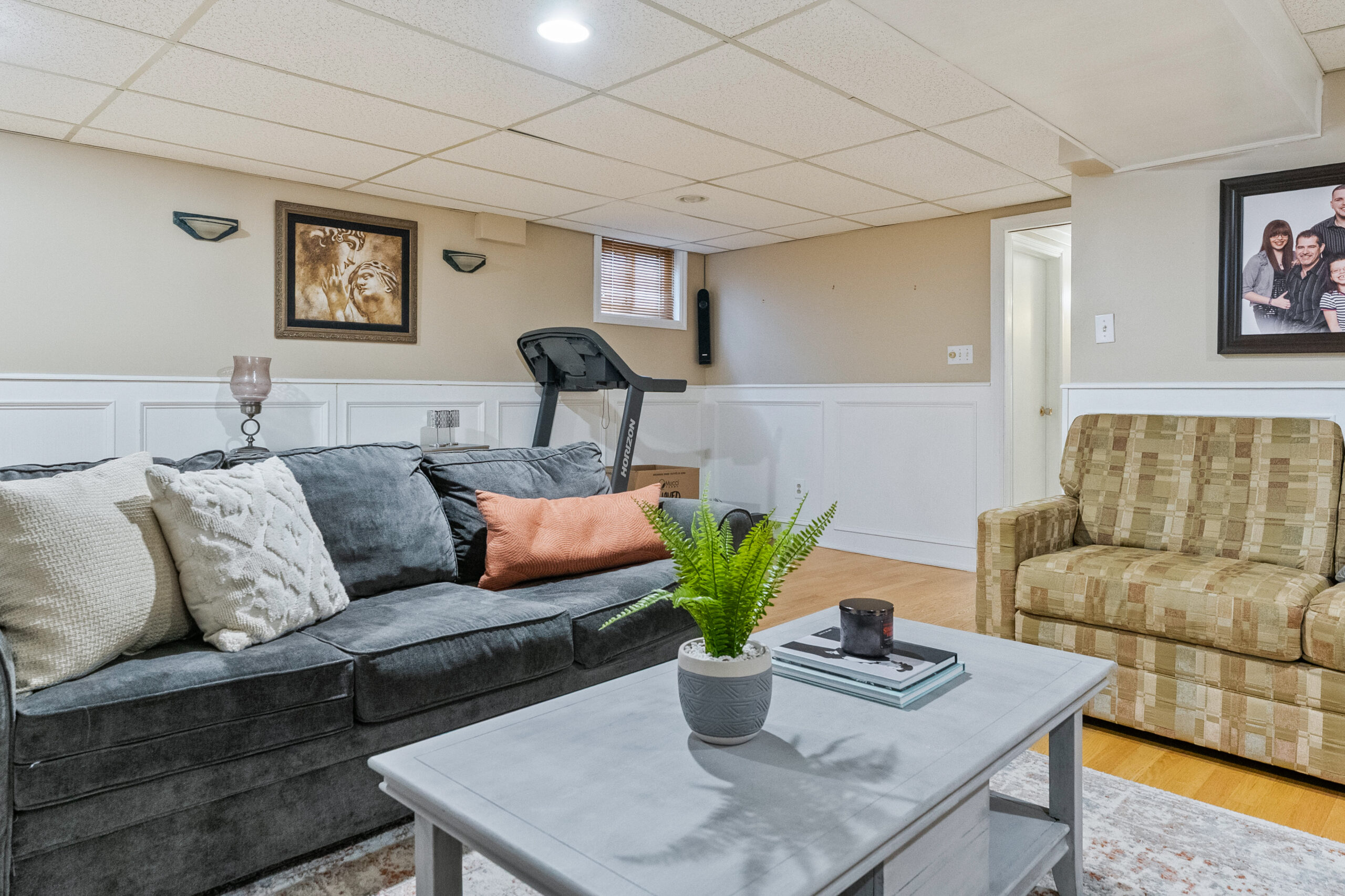 Cozy basement living area with a gray sofa, armchair, and treadmill
