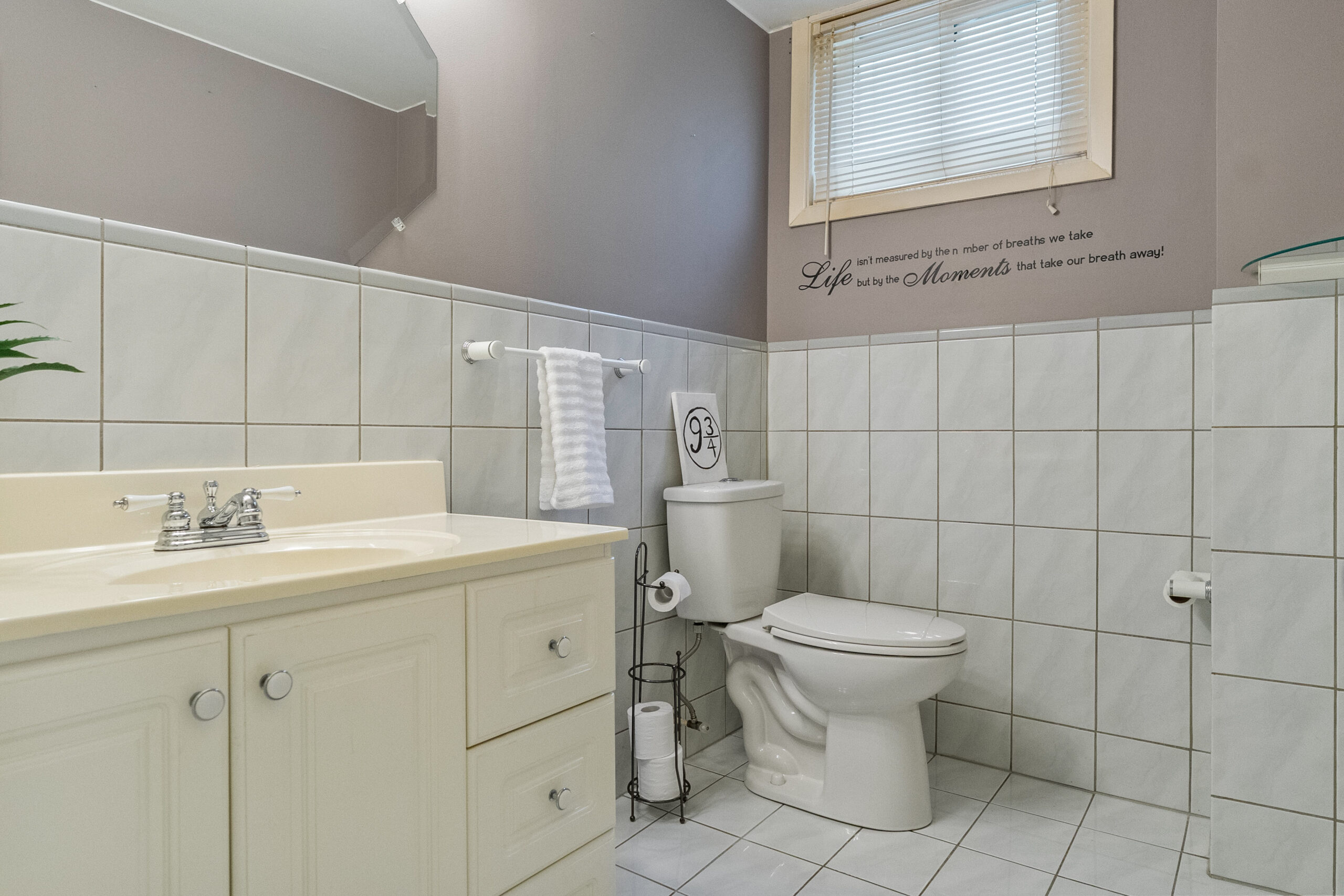Modern bathroom with beige cabinets, white tiles, and a window.
