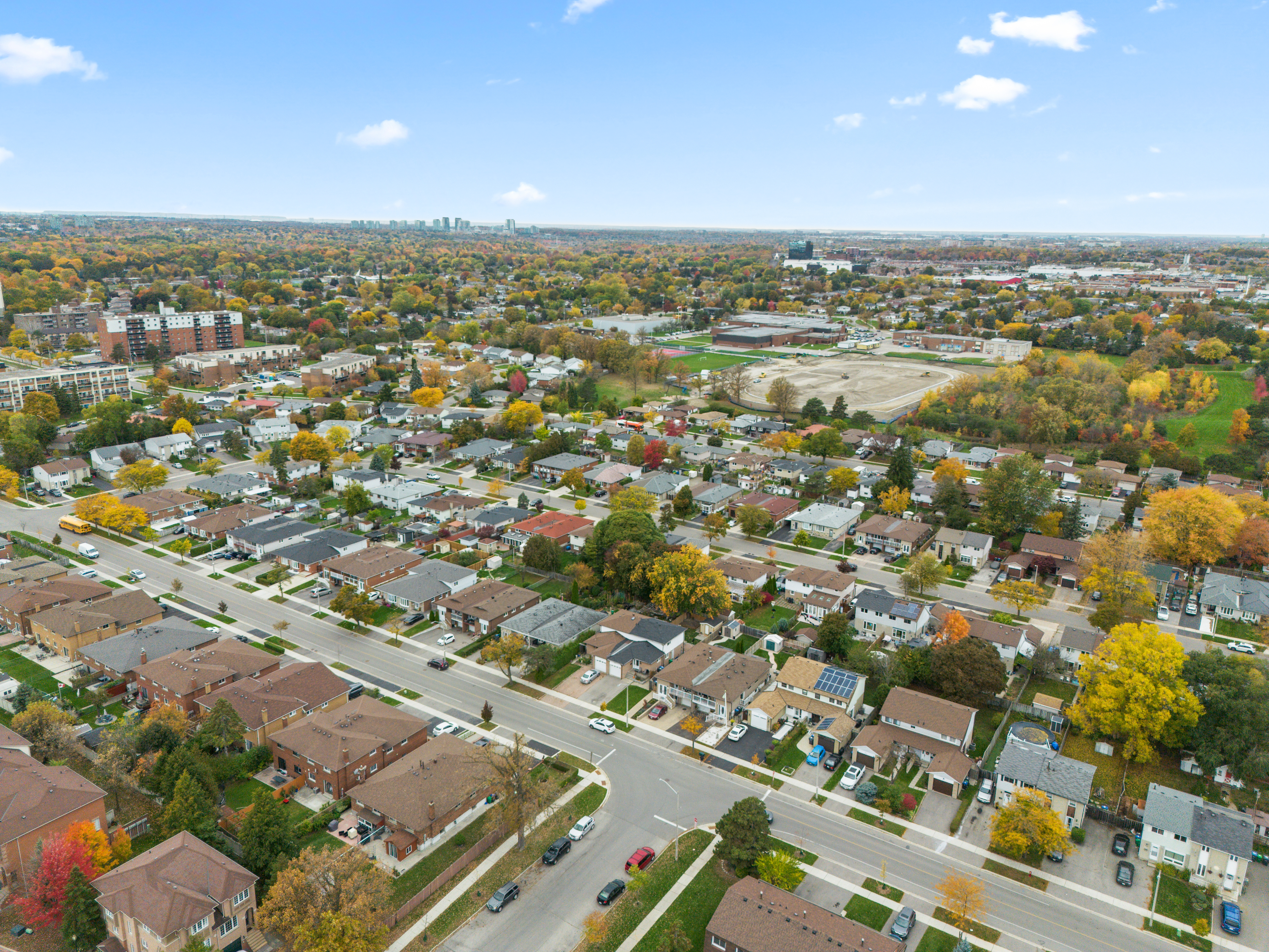 Aerial view of suburban neighborhood with autumn foliage and city skyline in distance