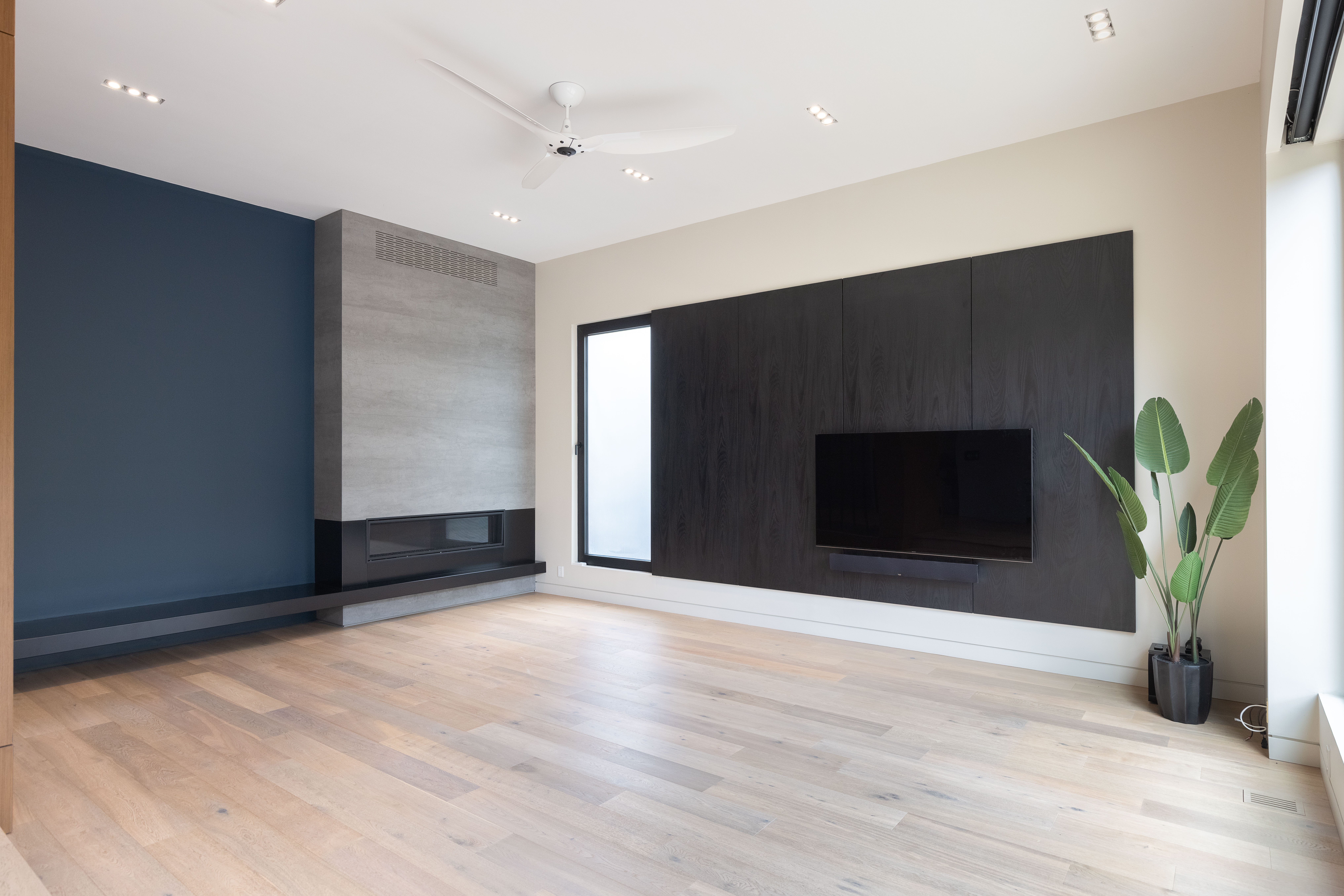 Modern living room with hardwood floors, wall-mounted TV, and indoor plant