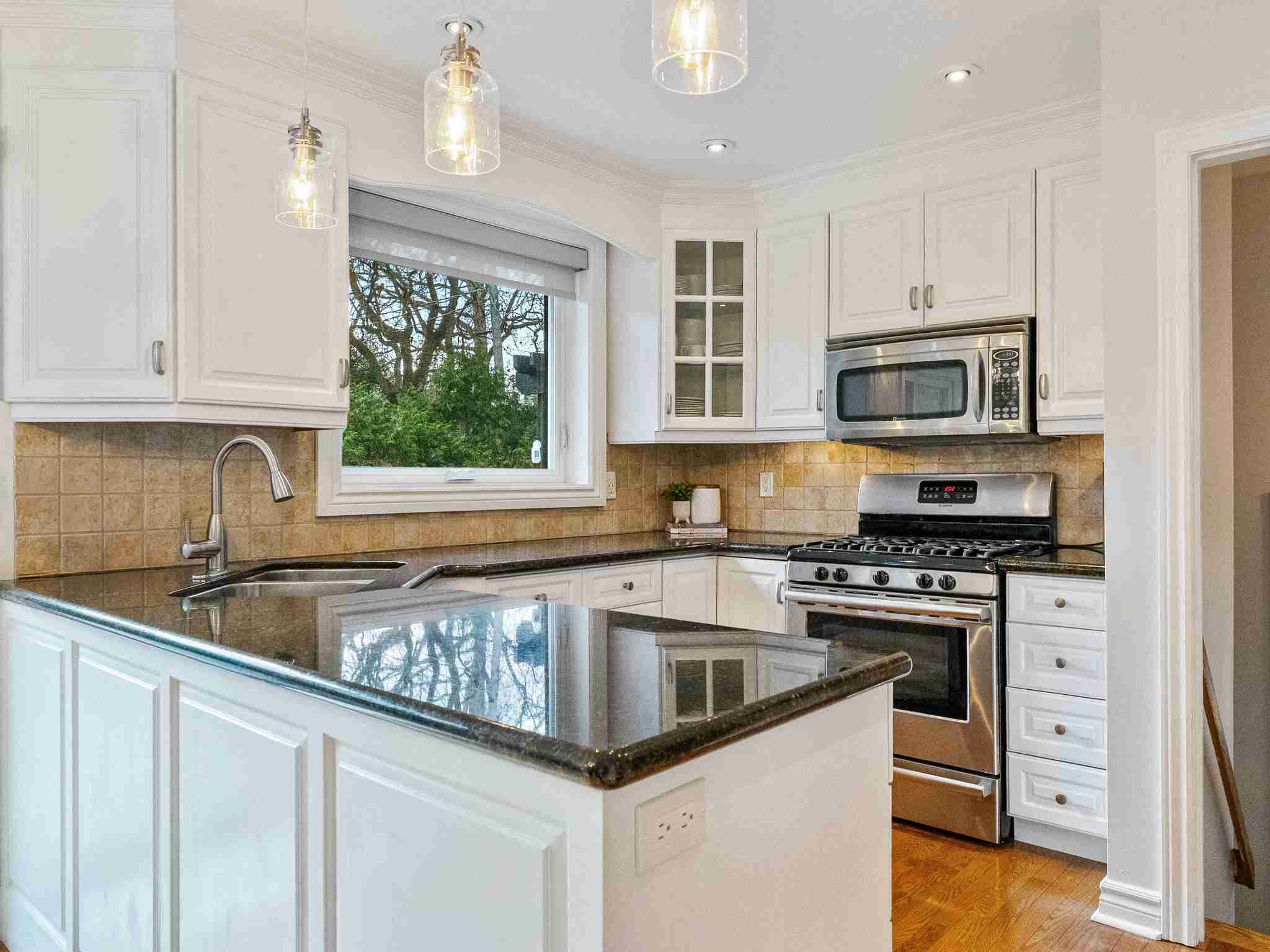 updated kitchen with black counter tops and stainless steel appliances