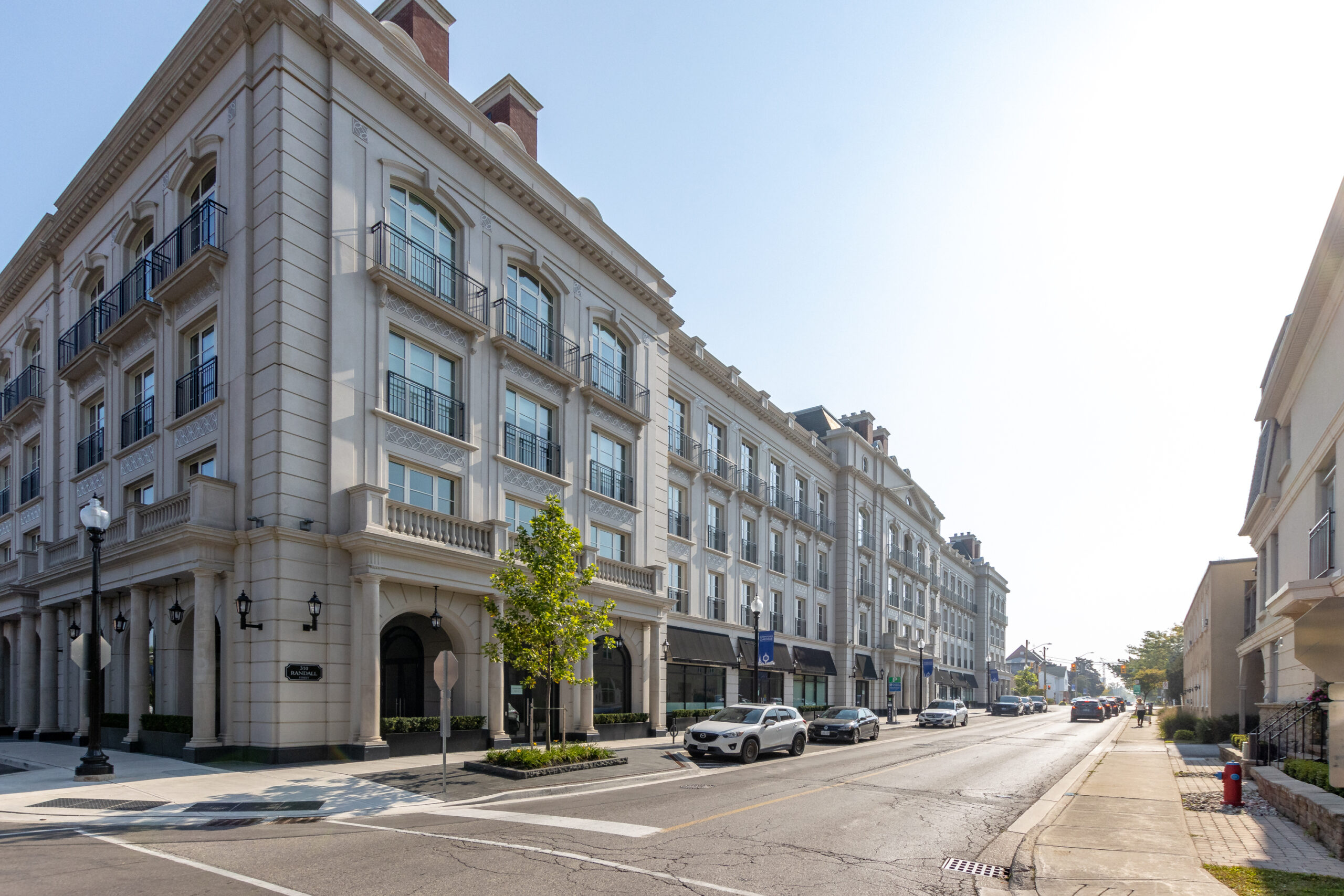Modern buildings lining a sunny street with parked cars and trees
