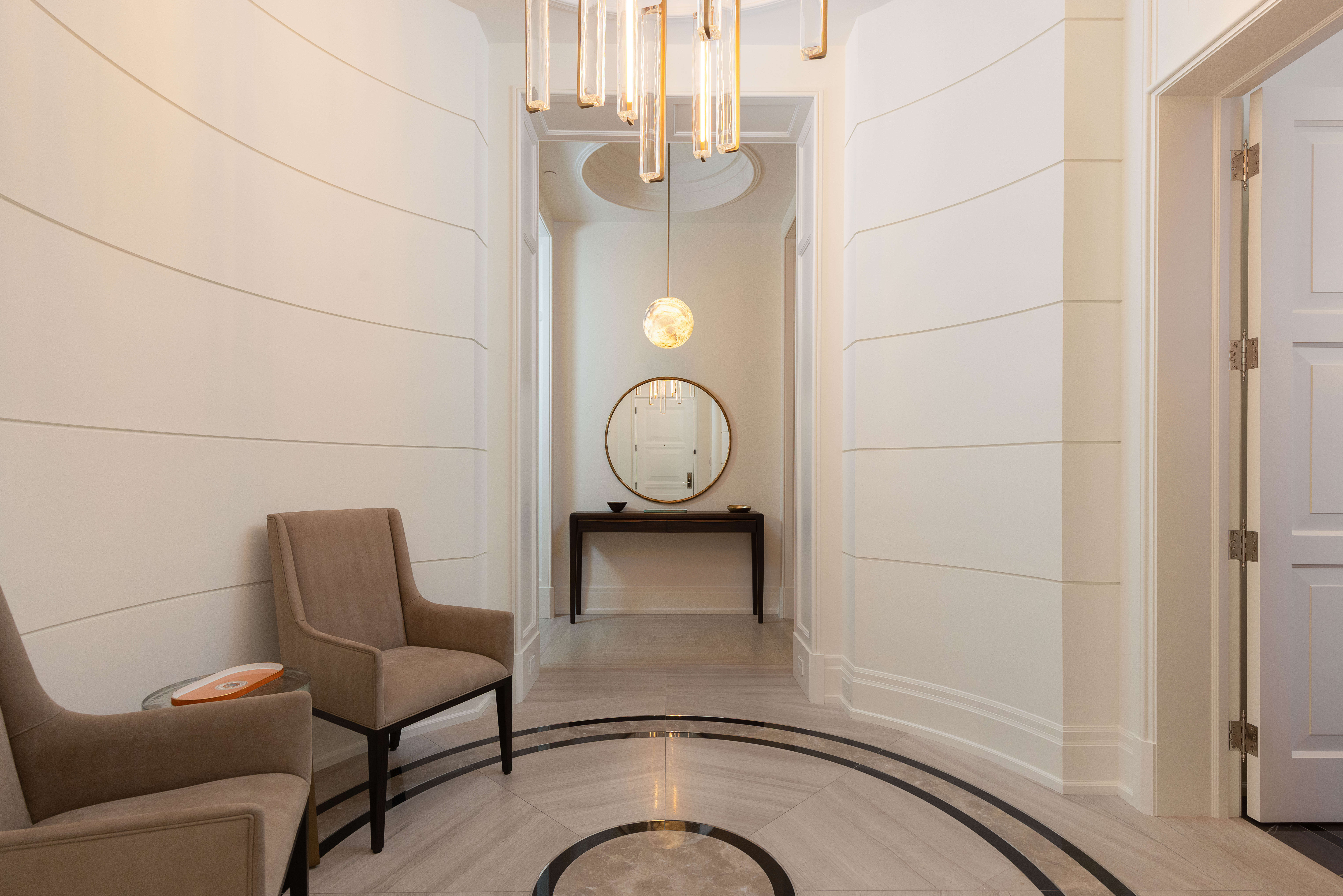 Elegant hallway with two chairs, round mirror, and modern lighting fixtures