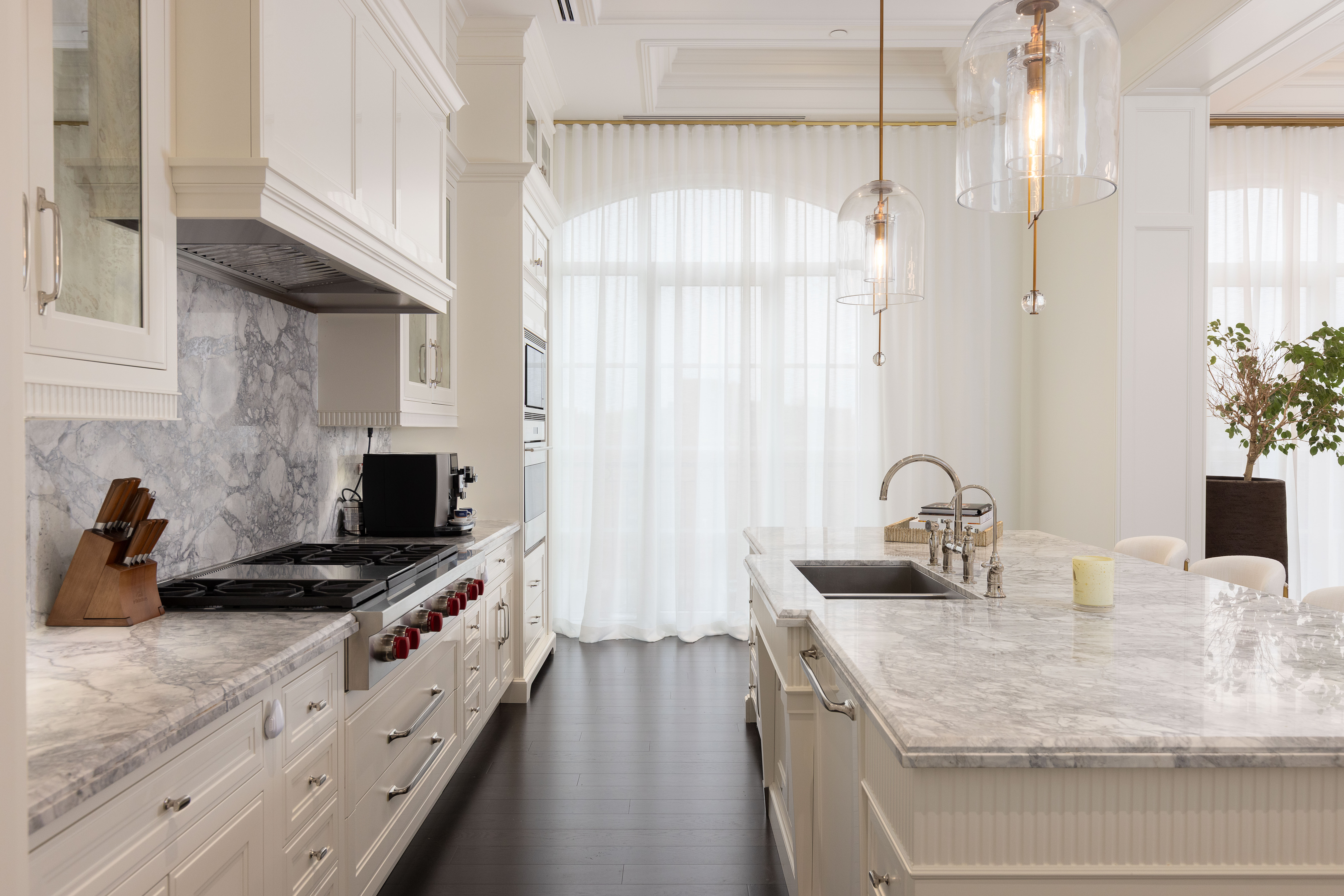 Modern kitchen with marble countertops, white cabinetry, and large windows.
