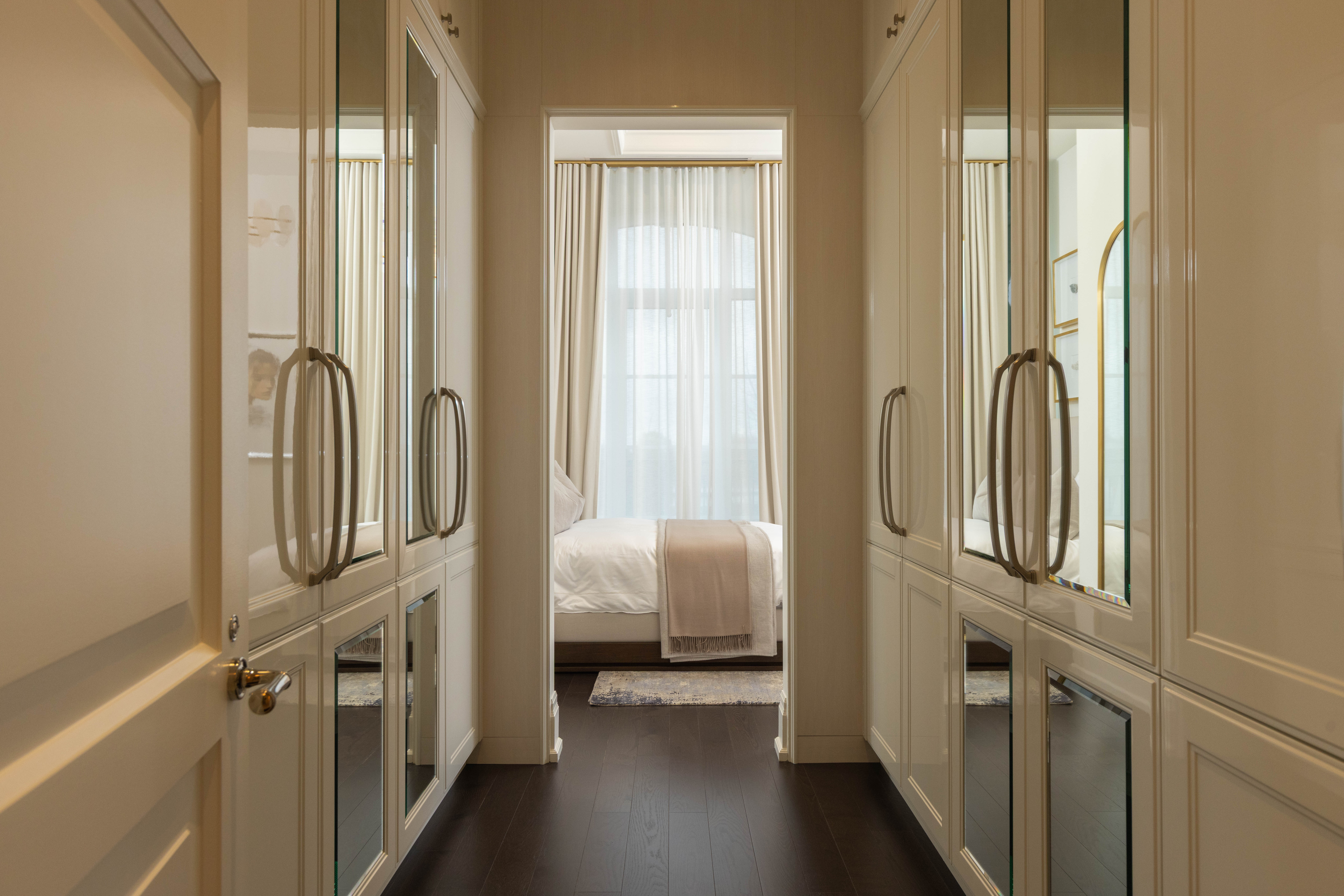 Narrow hallway with mirrored closet doors leading to a softly lit bedroom