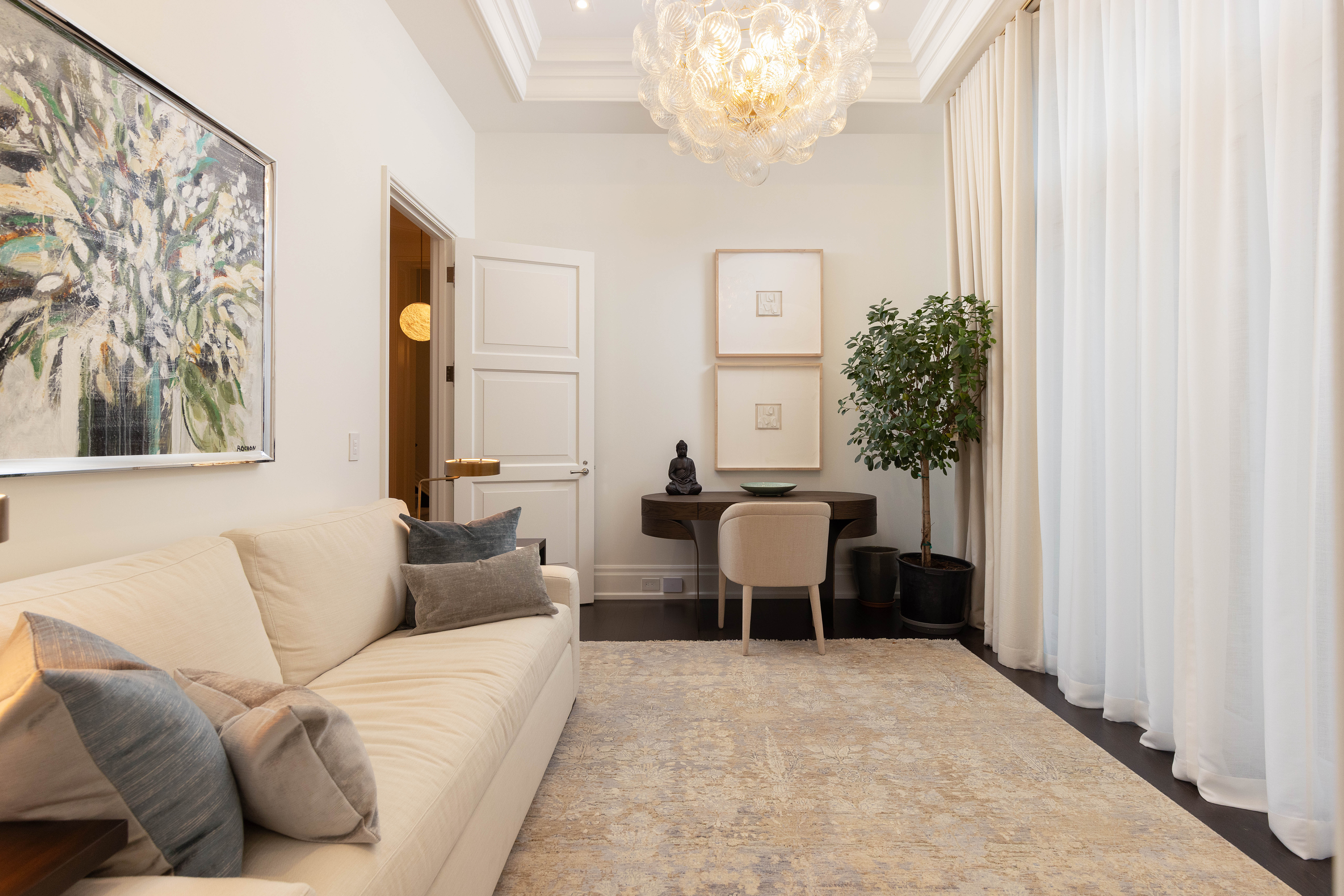 Modern living room with a beige sofa, artwork, and a desk by a window