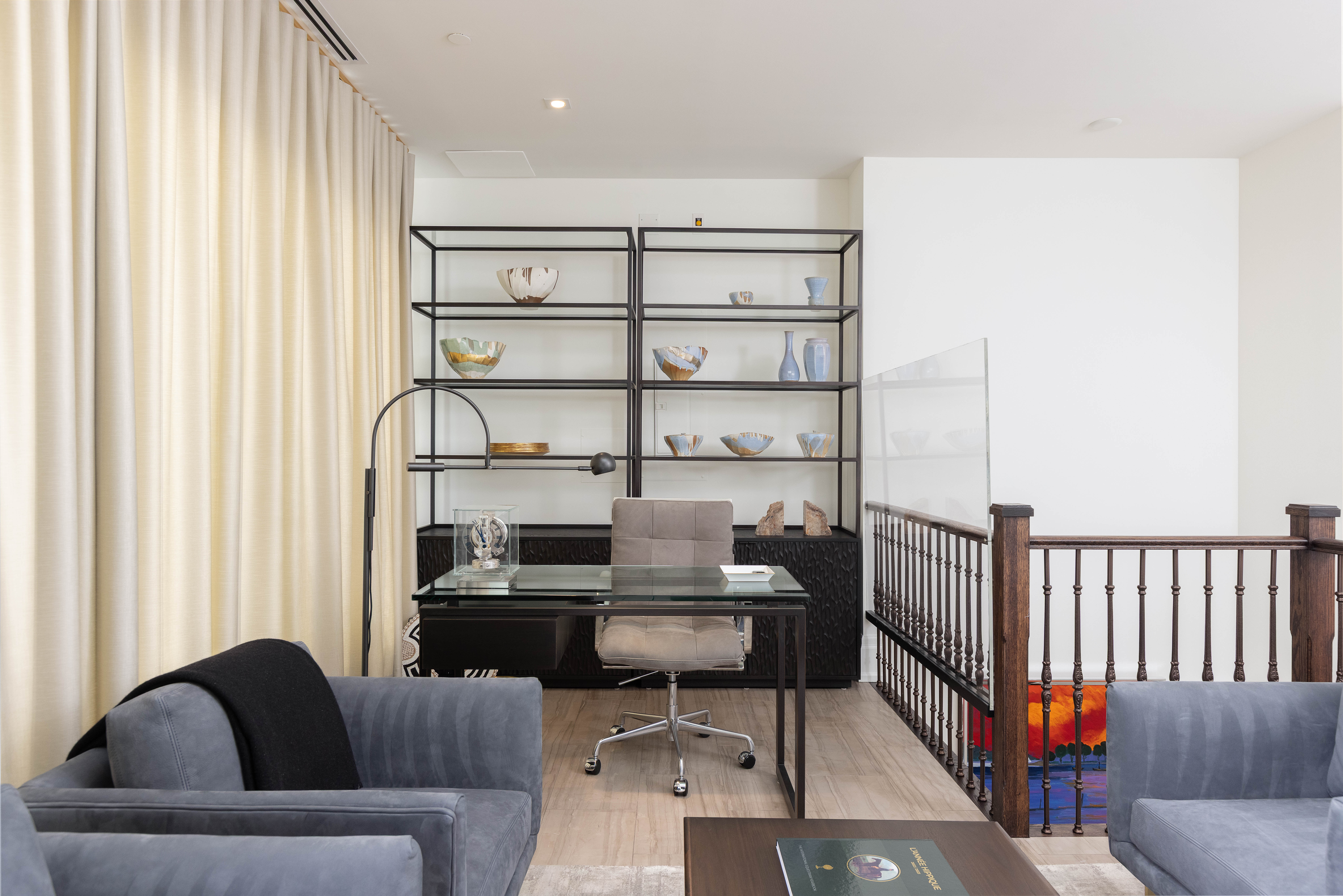 Modern office space with a glass desk, gray chairs, and decorative shelves
