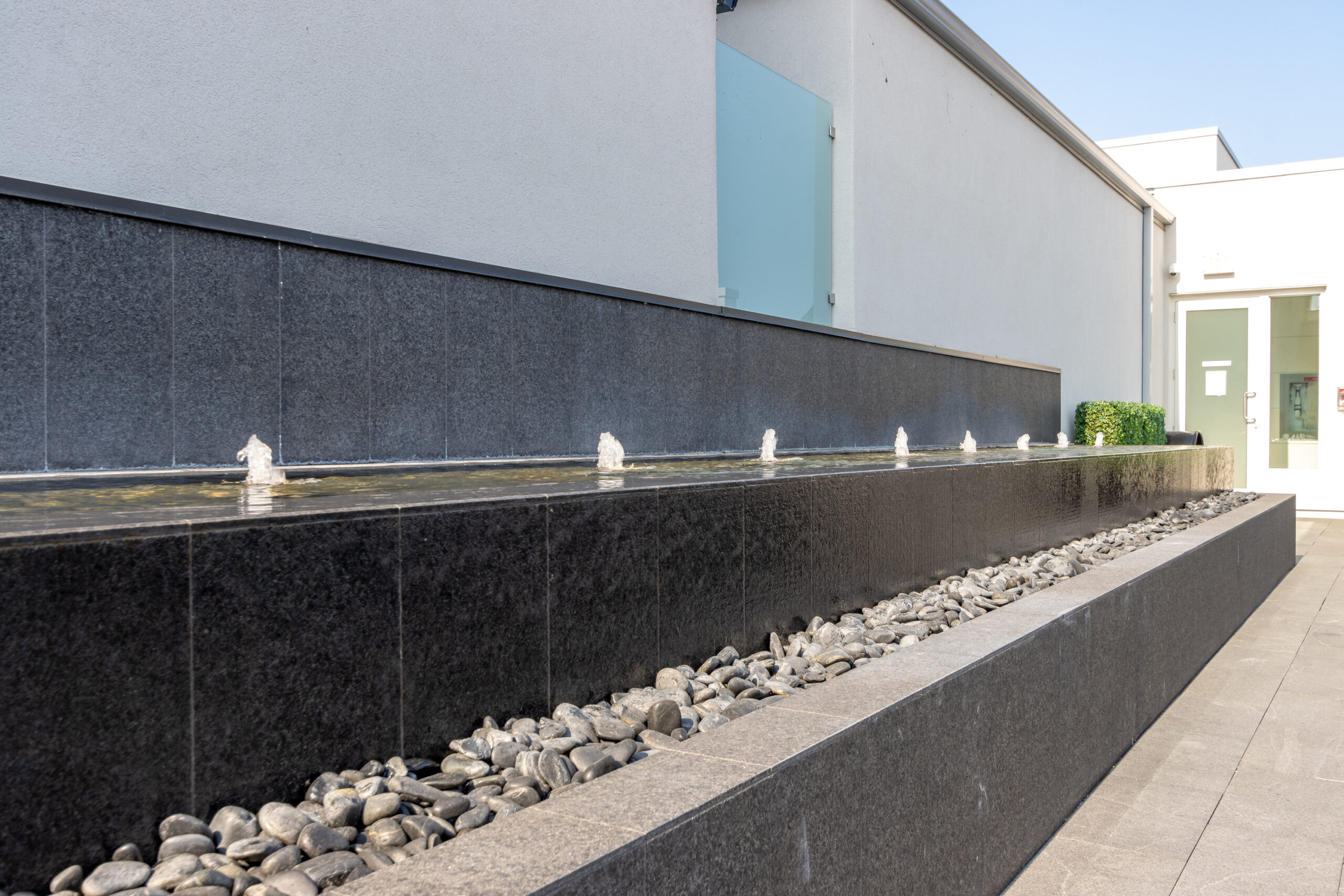Modern water feature with small fountains and pebbles along a stone wall