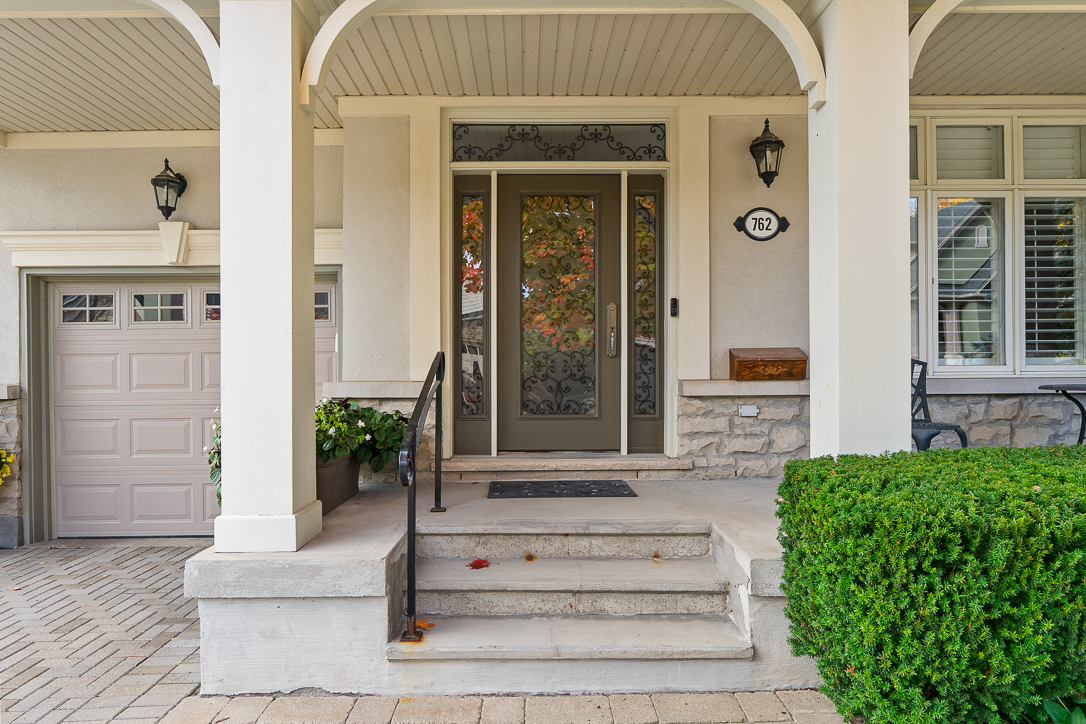 Front porch with steps, green bushes, and a decorative door.