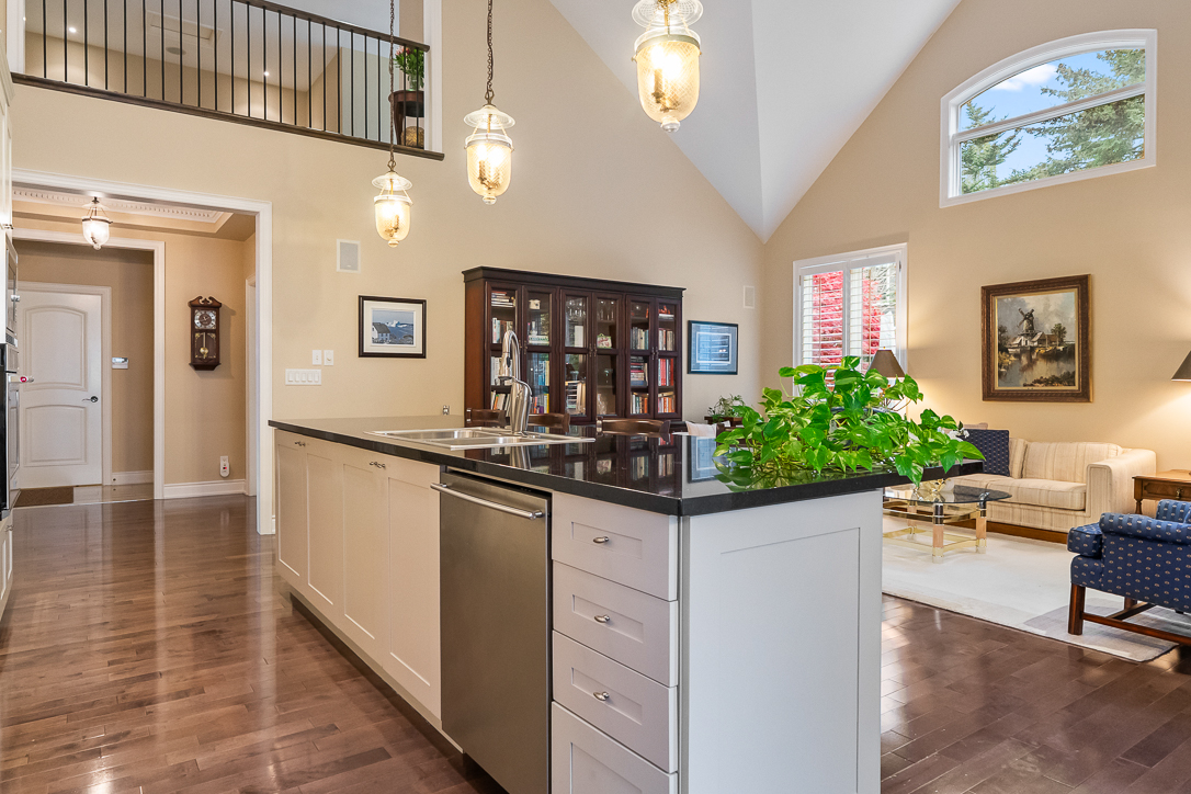 Bright kitchen with island, hardwood floors, and living area in background