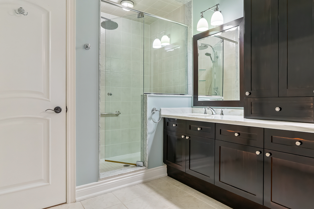 Modern bathroom featuring dark cabinetry, glass shower, and dual sinks
