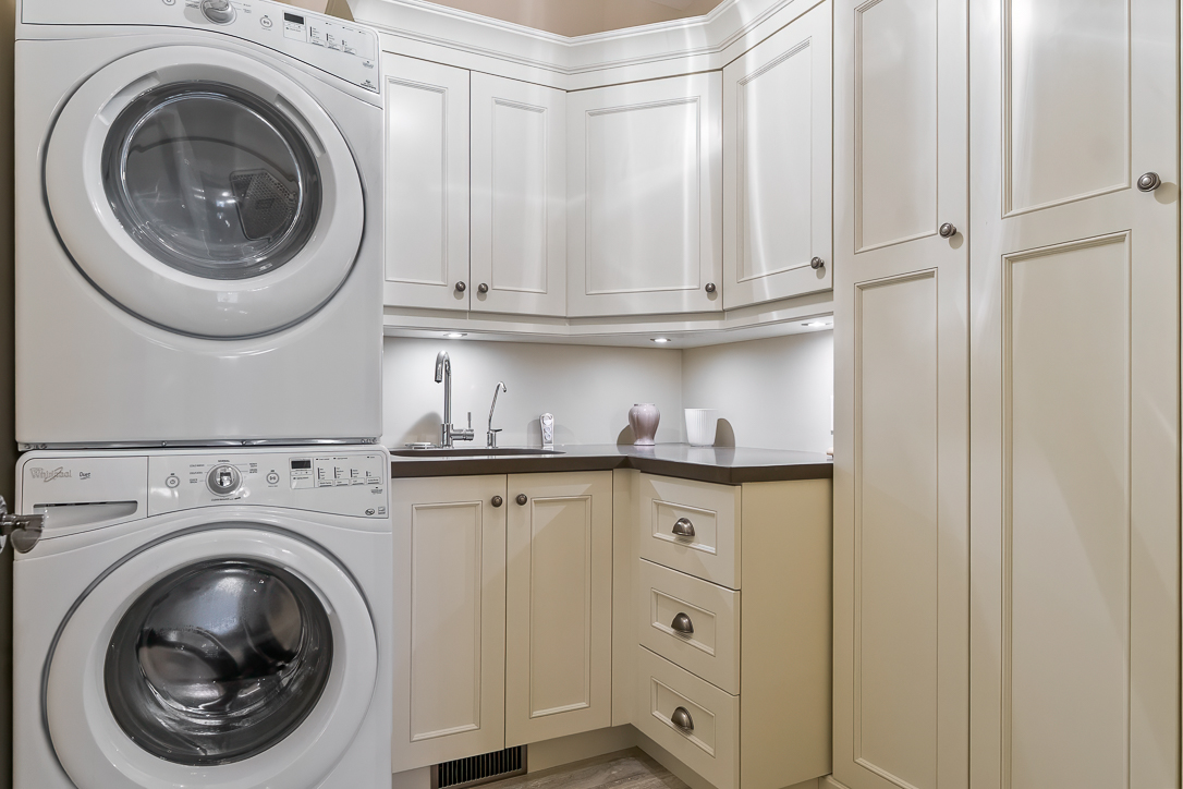 Modern laundry room with stacked washer and dryer, light cabinetry, and countertop