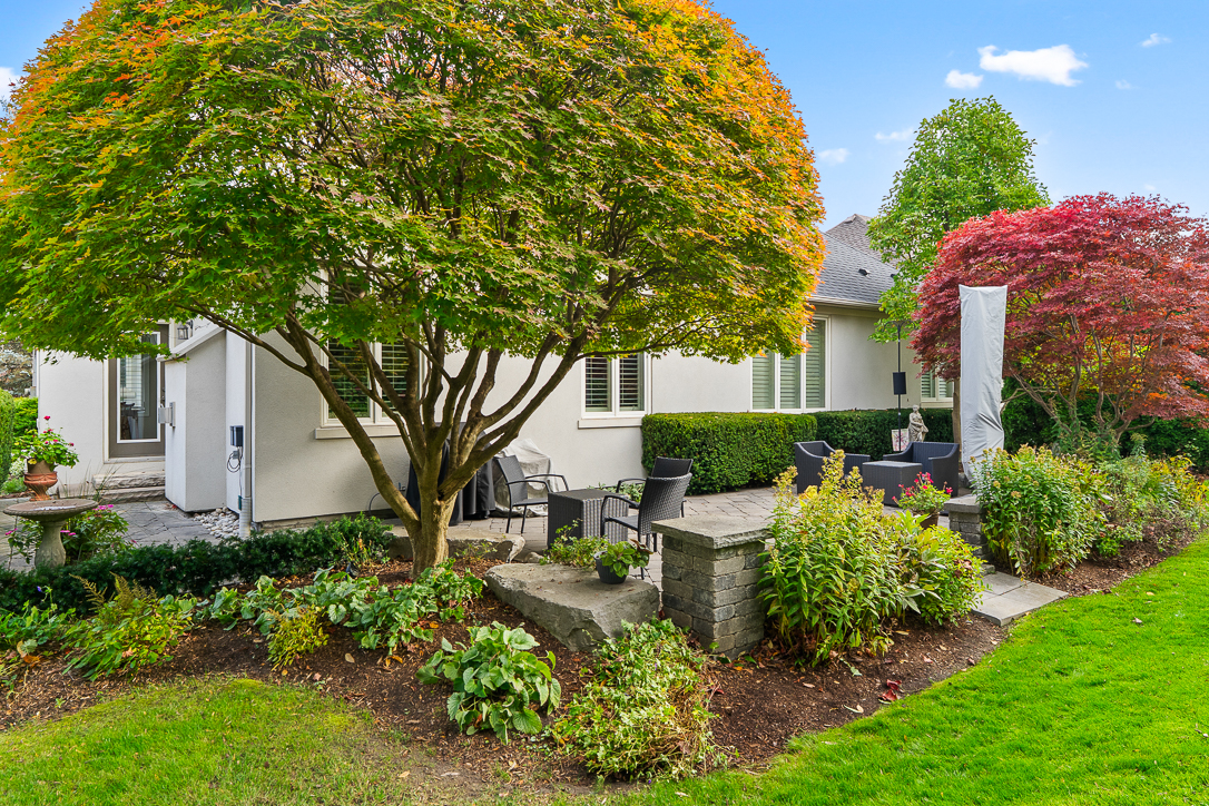 Lush garden with colorful trees and stone patio beside a house