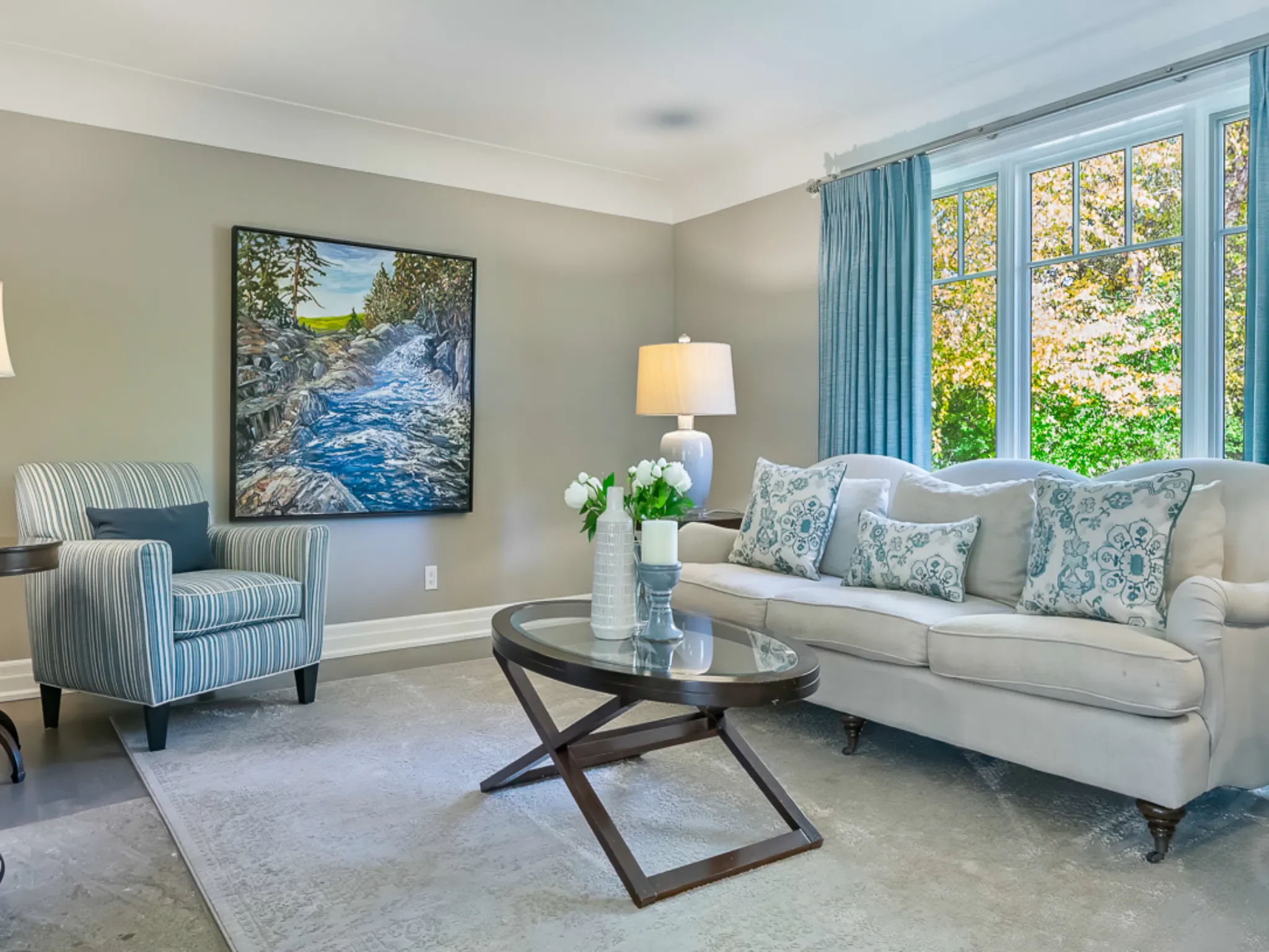 Cozy living room with a light sofa, artwork, and large windows