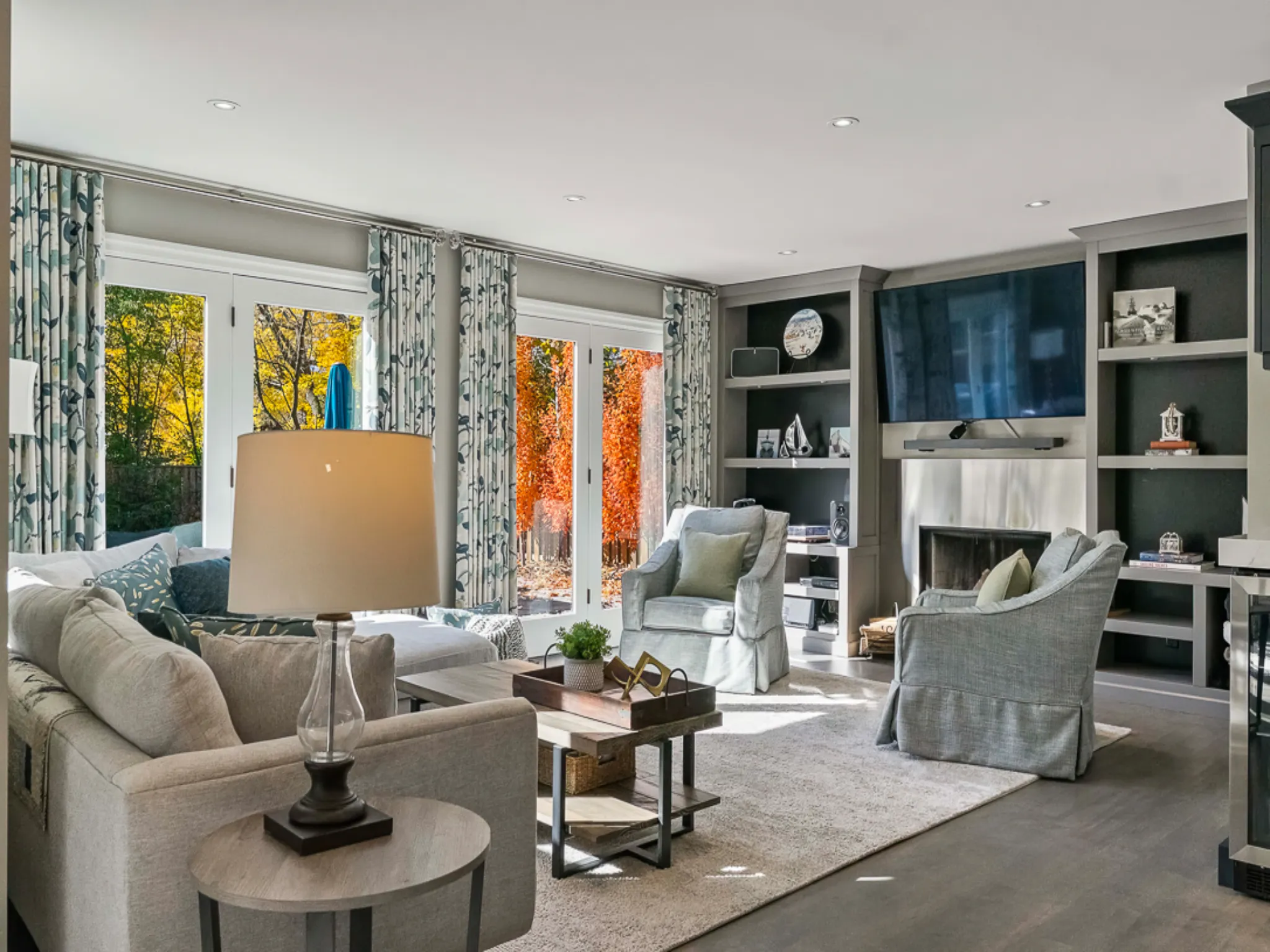 Cozy living room with large windows, modern furniture, and autumn foliage outside