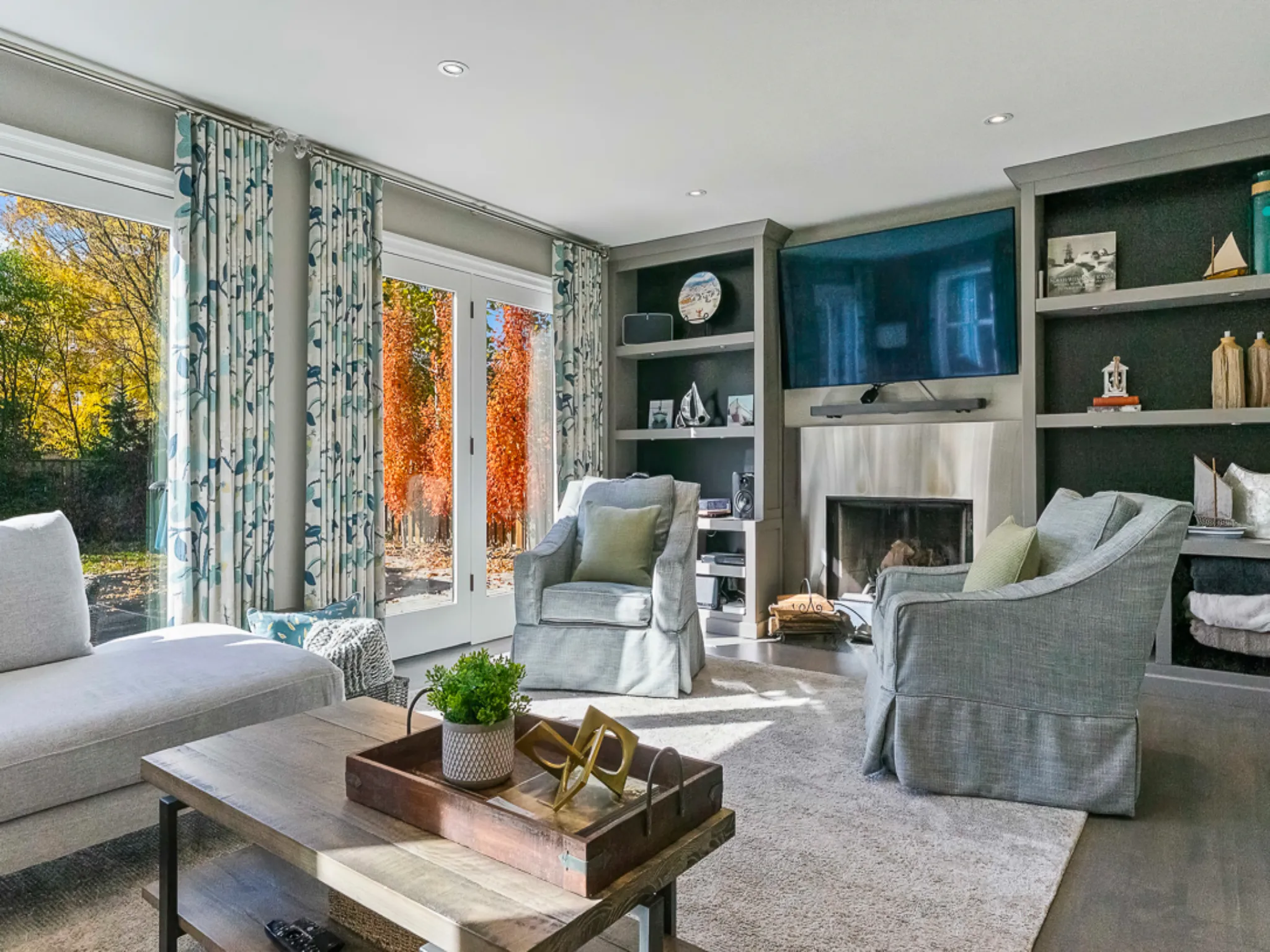 Bright living room with large windows, cozy seating, and decorative shelves