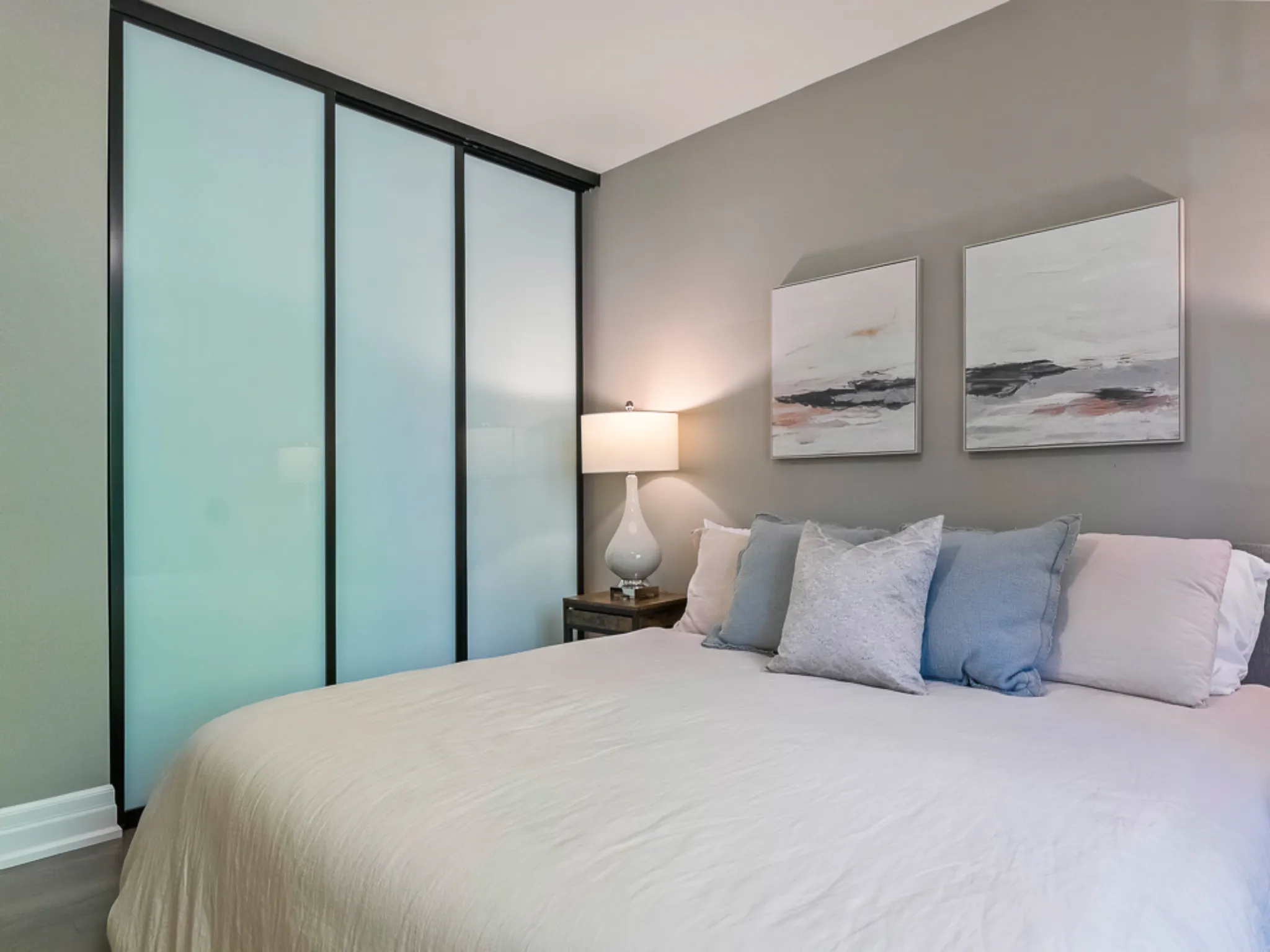 Modern master bedroom with a bed, decorative pillows, and sliding glass closet doors