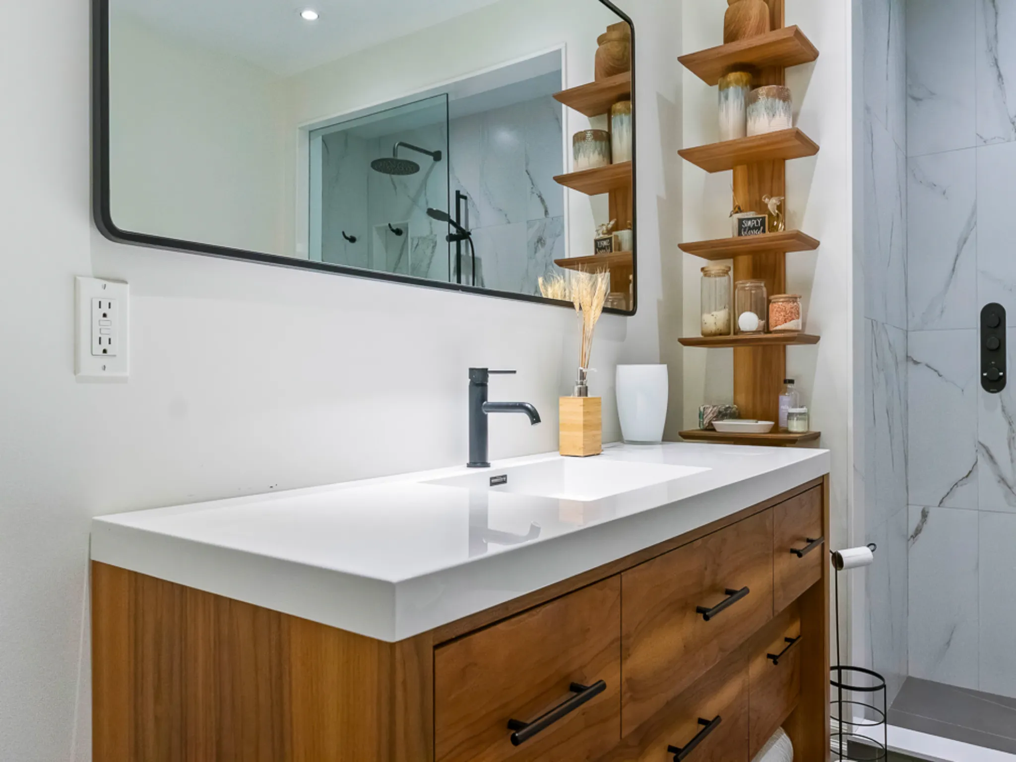 Modern master bathroom with wooden vanity, mirror, and decorative shelves