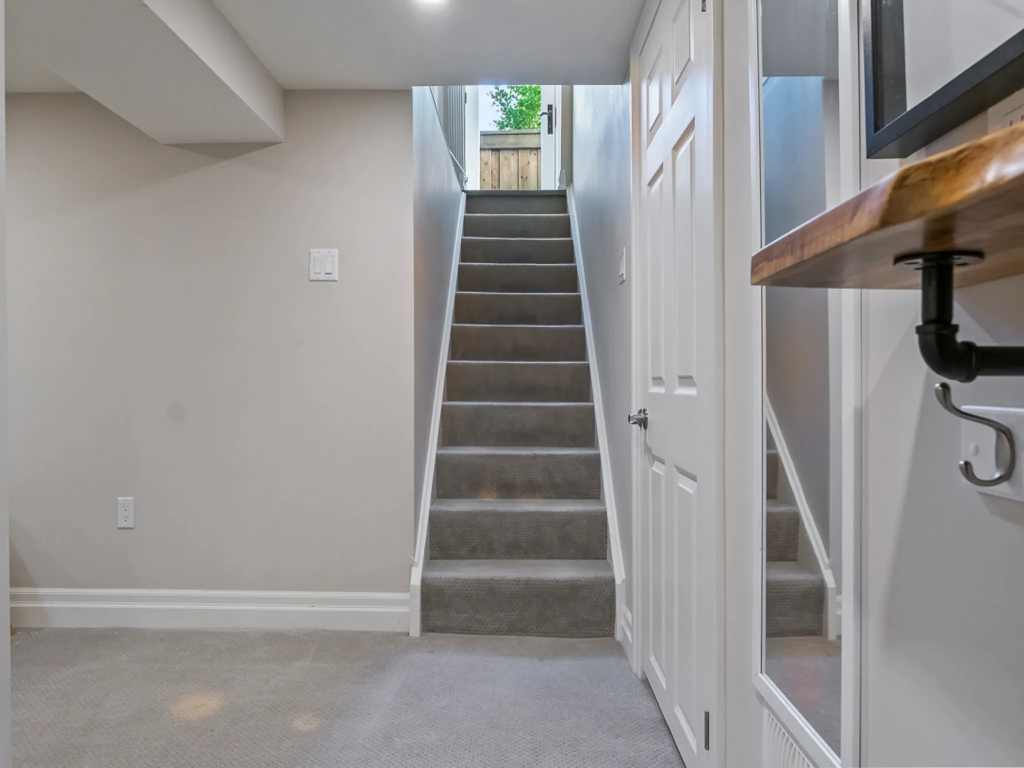 Basement hallway with carpeted stairs leading to a door and natural light