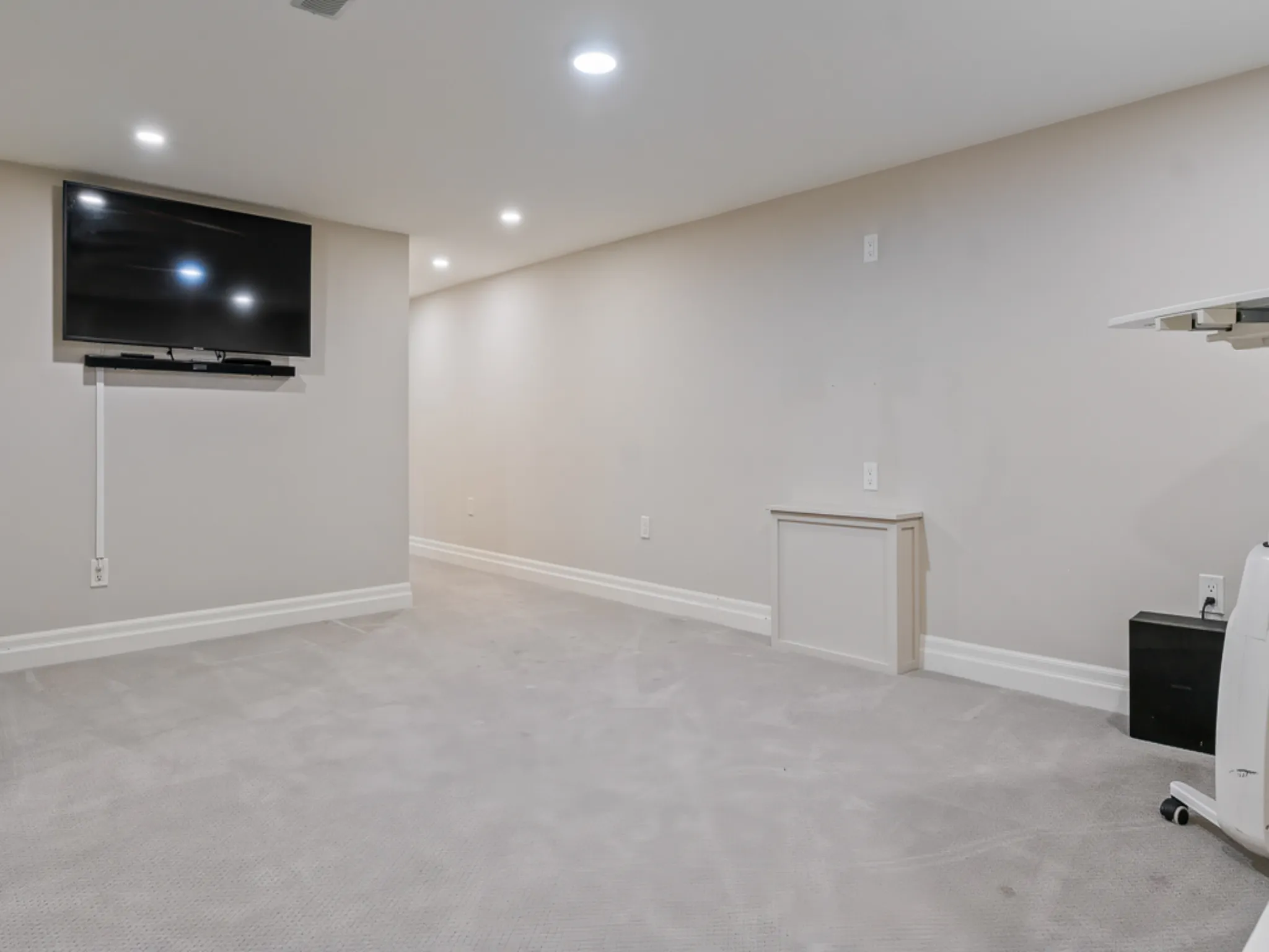 Spacious basement room with carpet, wall-mounted TV, and neutral walls