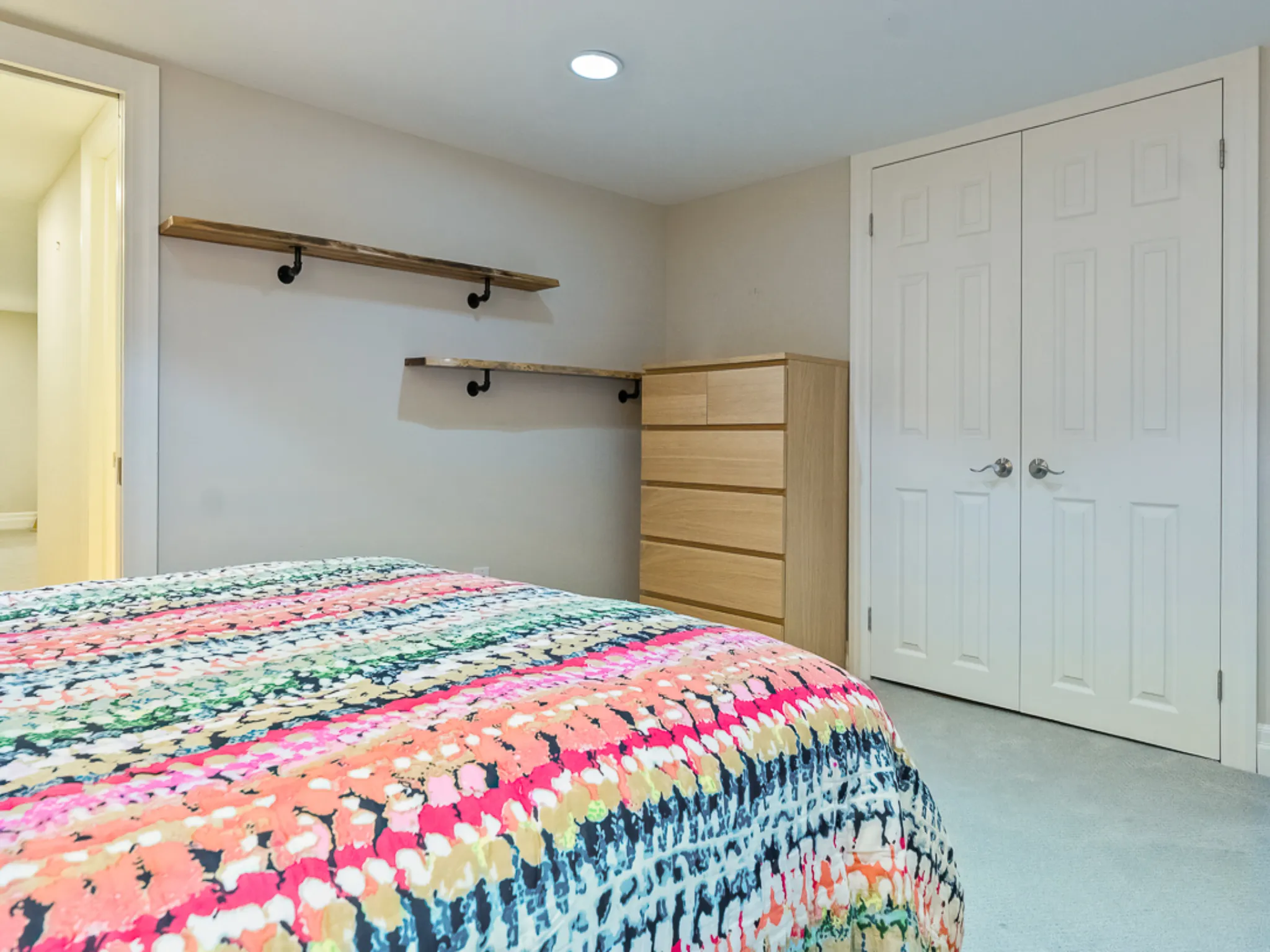 Colorful bedspread in a guest bedroom with dresser and shelves