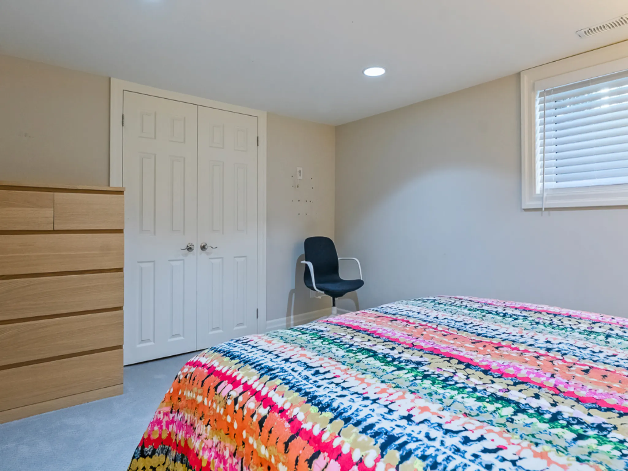 Colorful quilt on a bed in a cozy guest bedroom with a dresser and chair