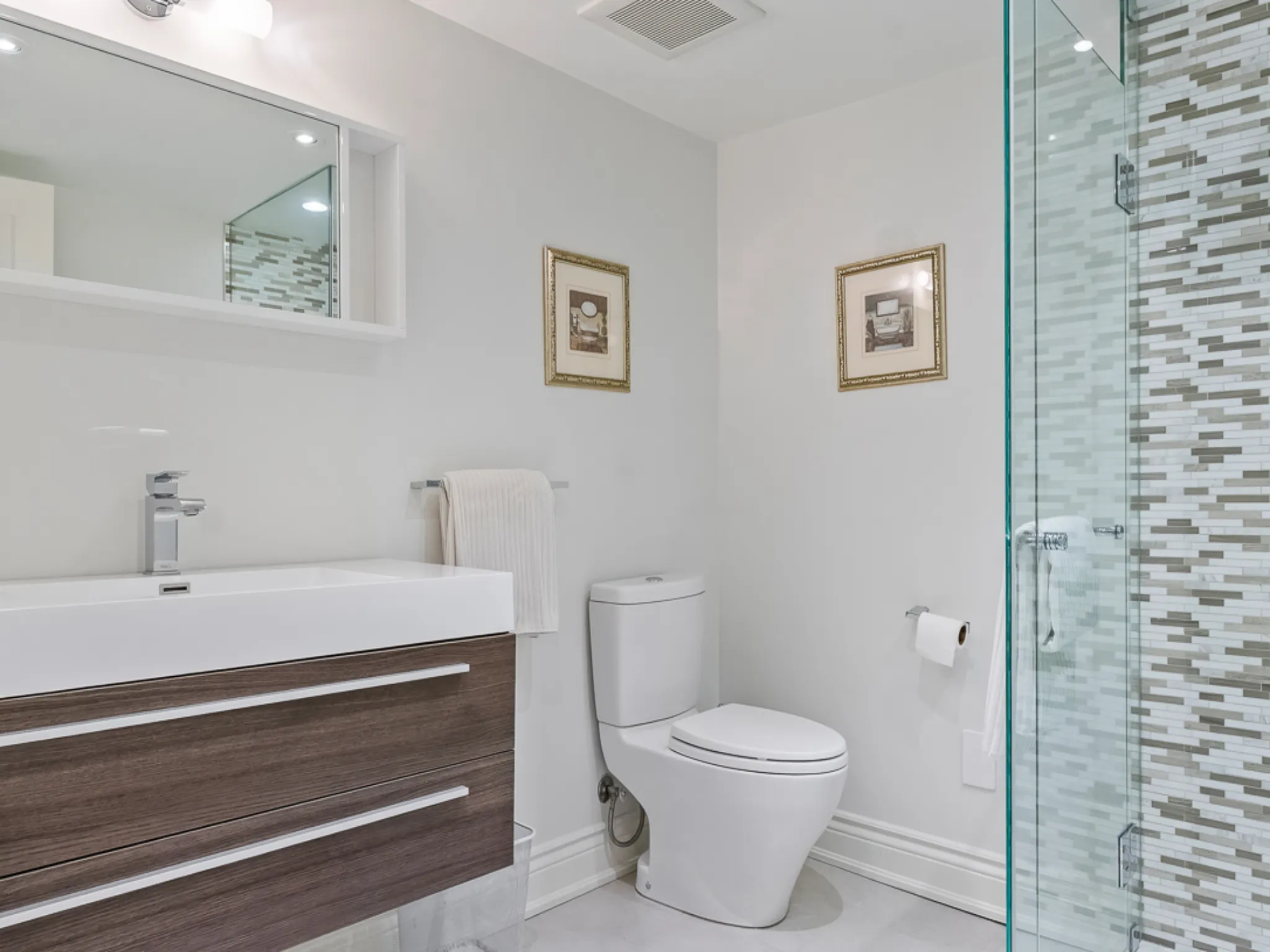 Modern bathroom with glass shower, wooden vanity, and decorative wall art