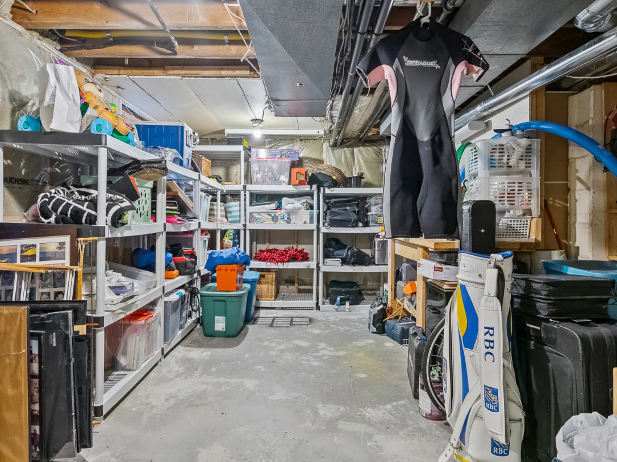 Cluttered storage room with shelves, bins, and a wetsuit hanging