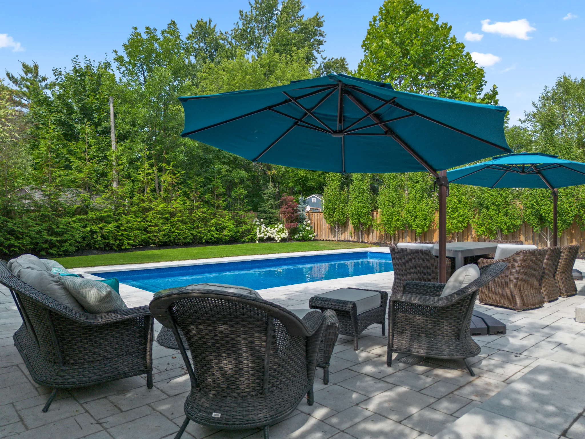 Outdoor seating area with umbrellas beside a swimming pool and greenery