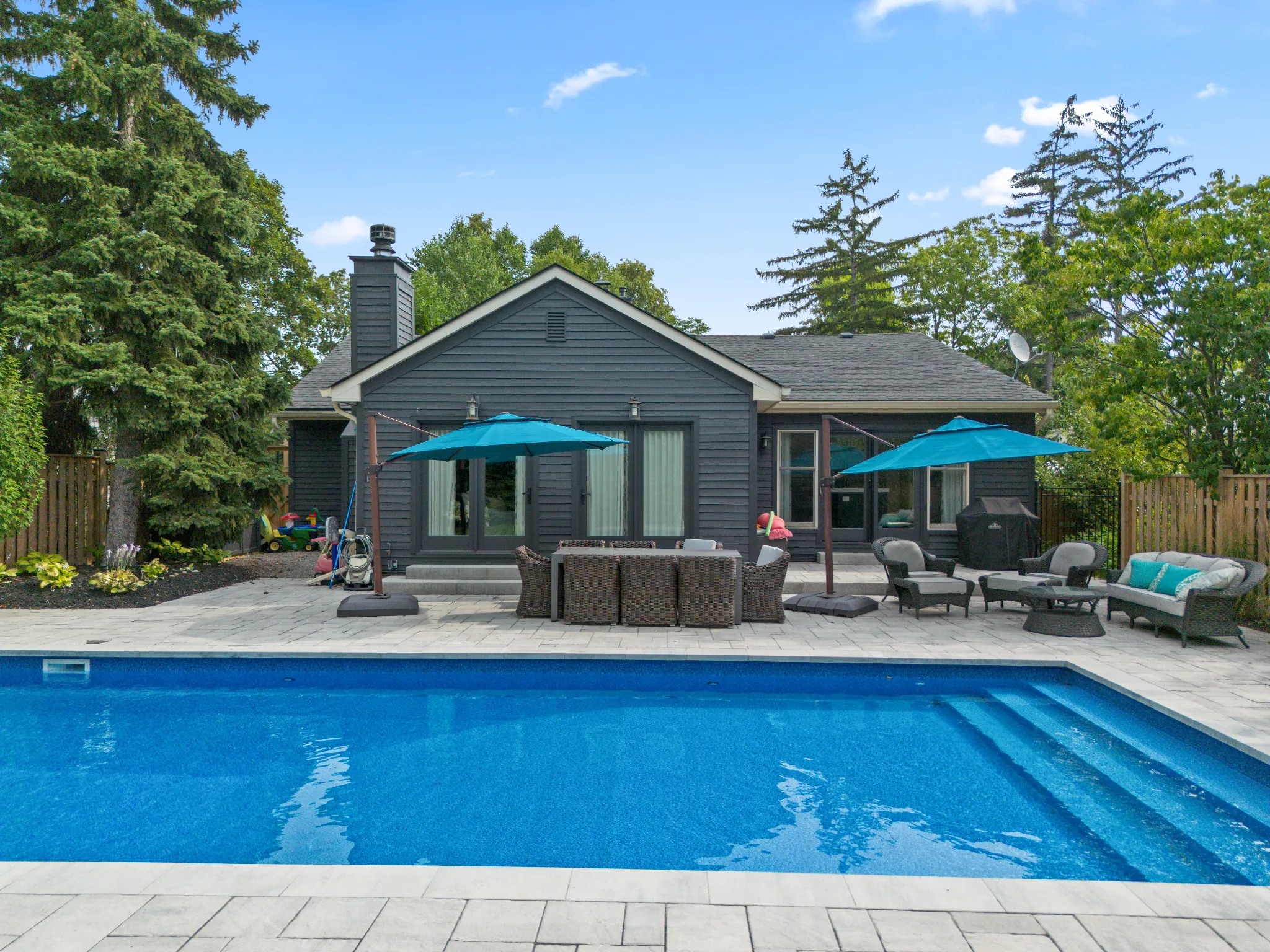 Modern home exterior with pool and patio furniture under blue umbrellas