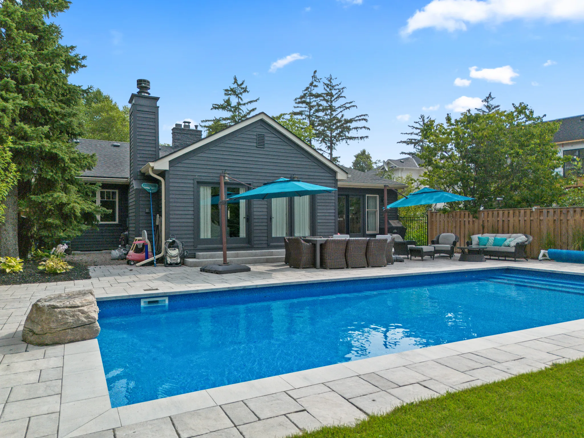 Modern home exterior with a pool, patio furniture, and umbrellas