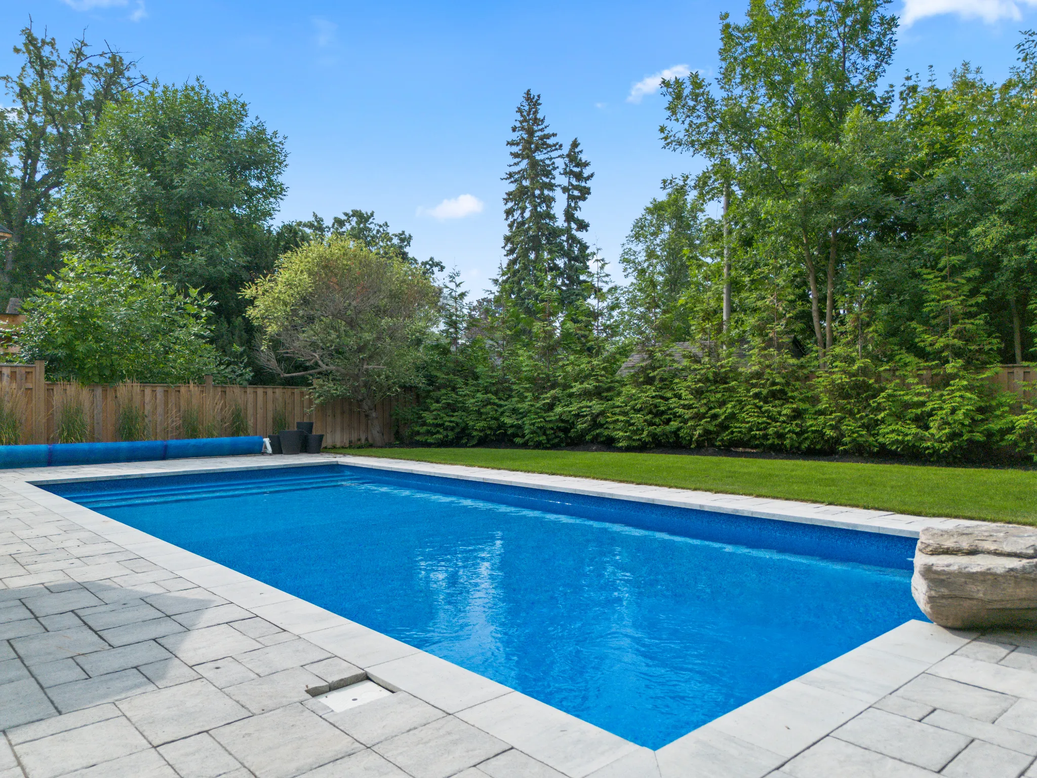 Backyard pool surrounded by greenery and stone patio