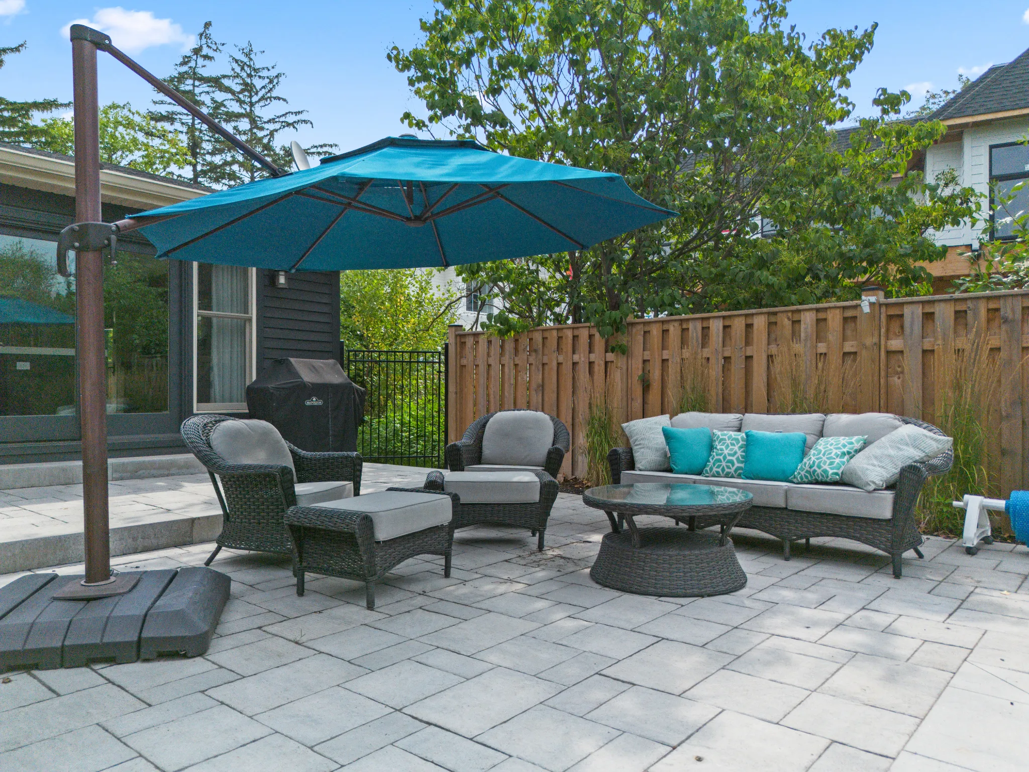 Patio area with teal umbrella, seating, and greenery in background