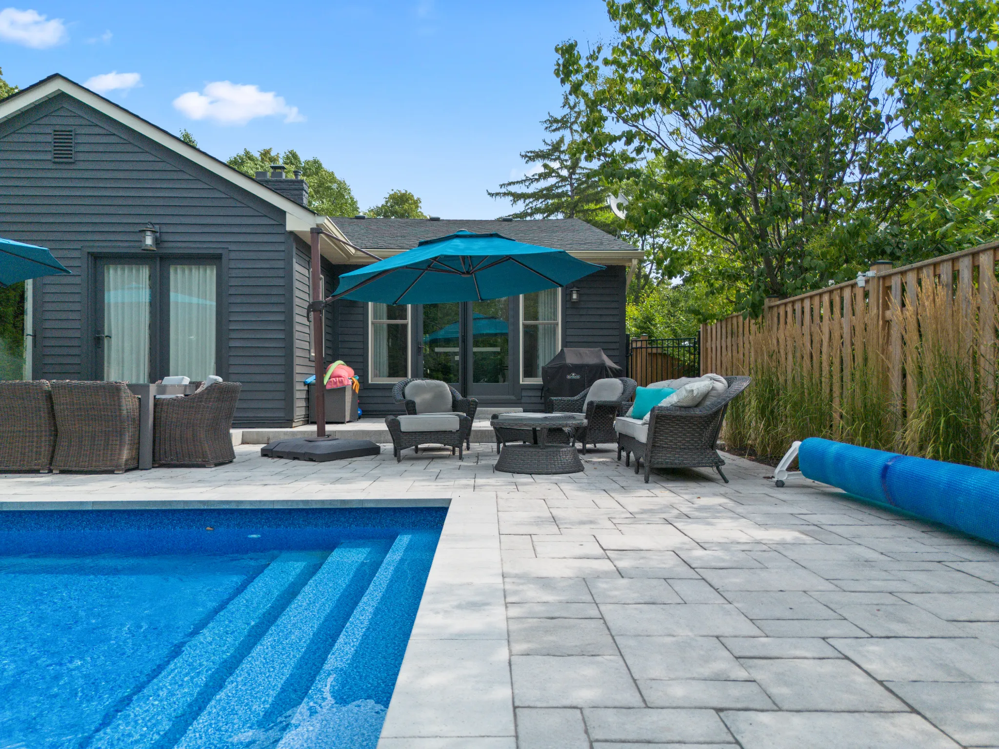 Backyard pool area with seating, umbrellas, and a modern home exterior