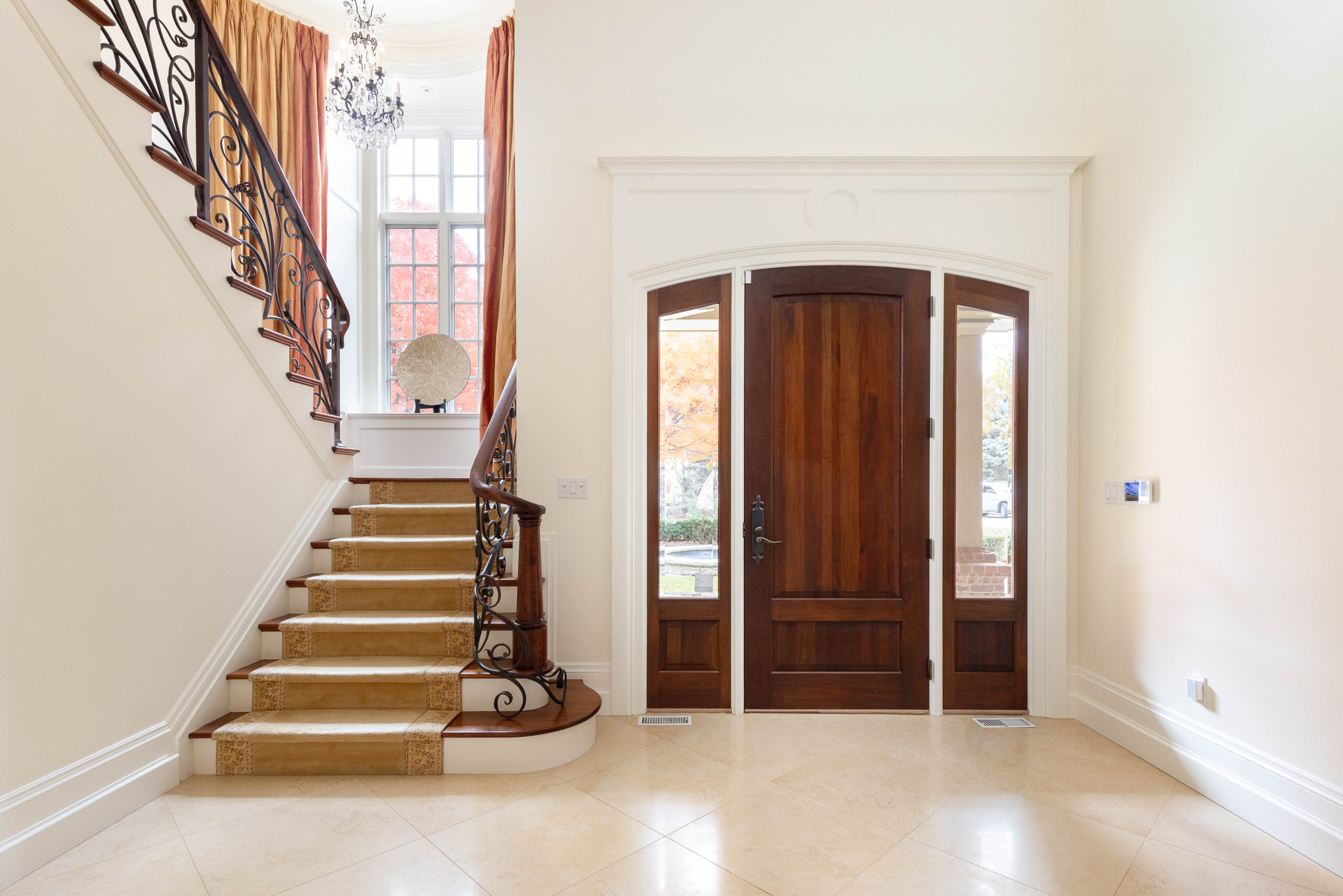 Elegant foyer with wooden doors and a staircase, featuring a chandelier.
